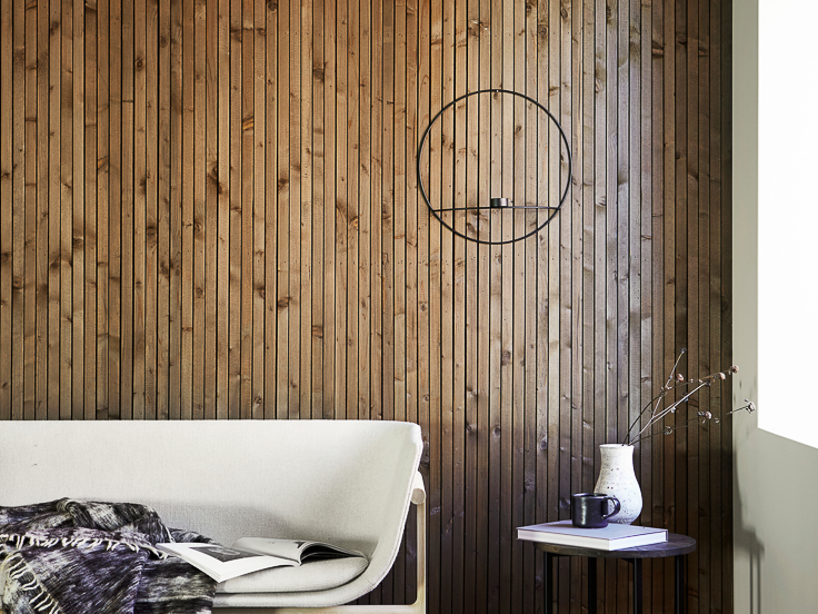 Vegg med smale spiler i tre beiset med mørk brun interiørbeis i fargen 9049 Valnøtt, hvit sofa foran veggen og vindu som slipper inn naturlig dagslys fra høyre