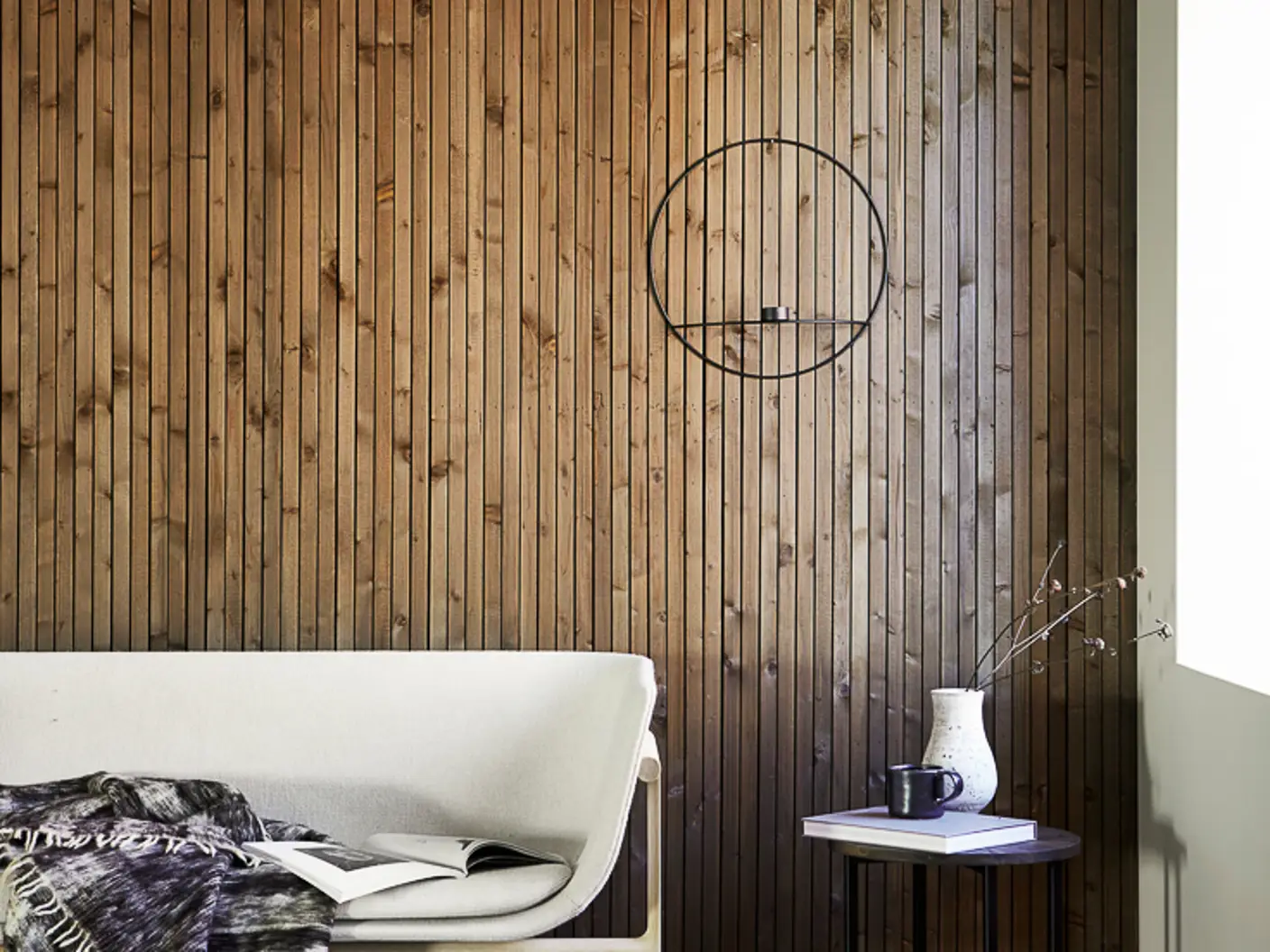 Vegg med smale spiler i tre beiset med mørk brun interiørbeis i fargen 9049 Valnøtt, hvit sofa foran veggen og vindu som slipper inn naturlig dagslys fra høyre