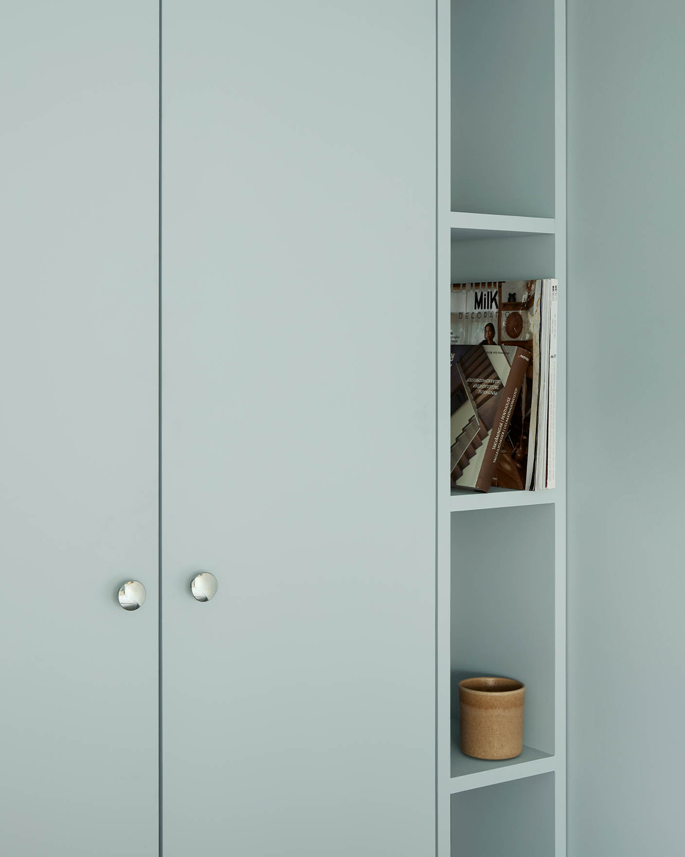 Cabinet painted in Jotun 6167 Spring Breeze with knobs; open shelves styled with magazines and a ceramic pot.