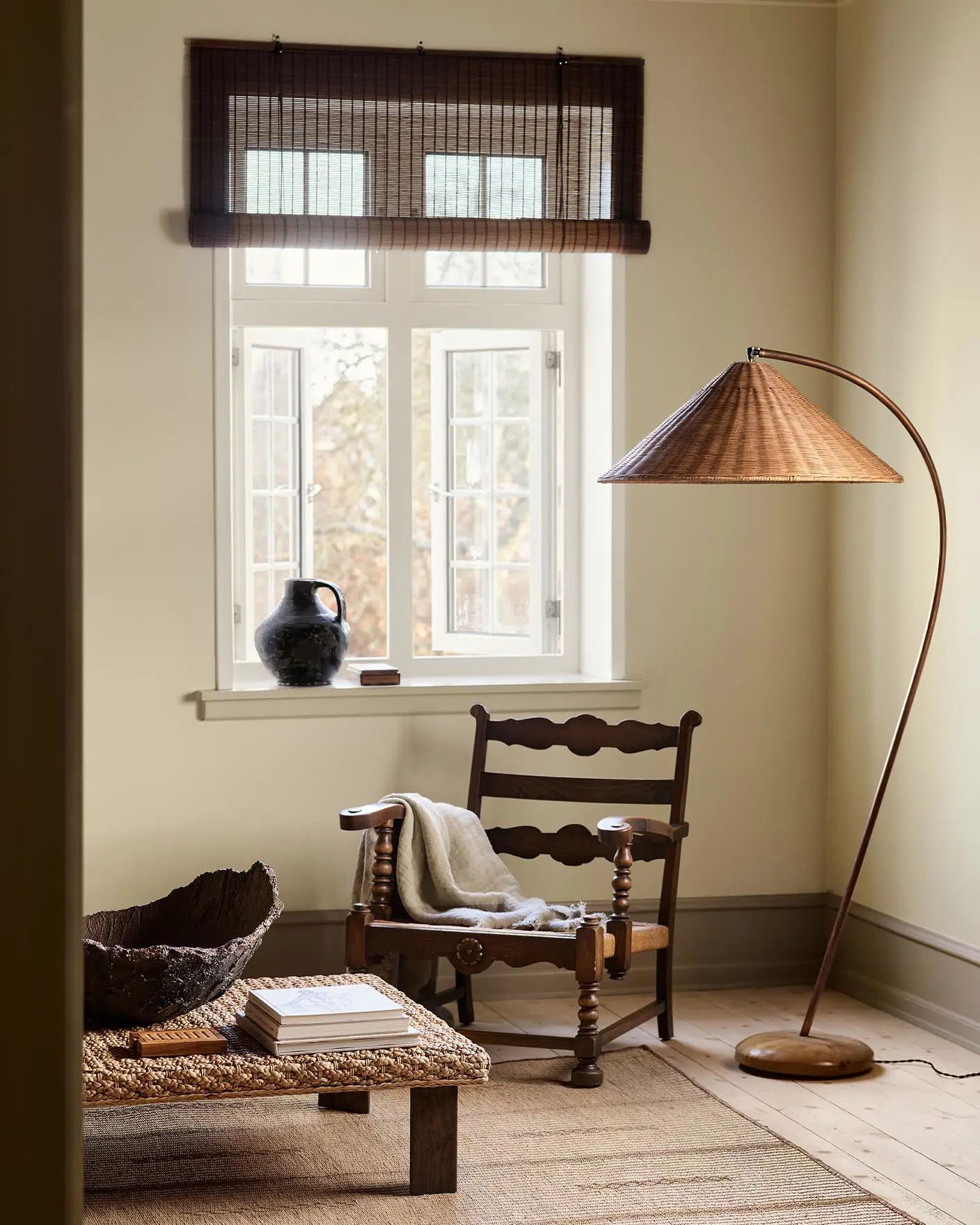 A wooden chair, woven lamp, and coffee table against a muted yellow wall painted in the colour 12080 Soft Radiance from Jotun.