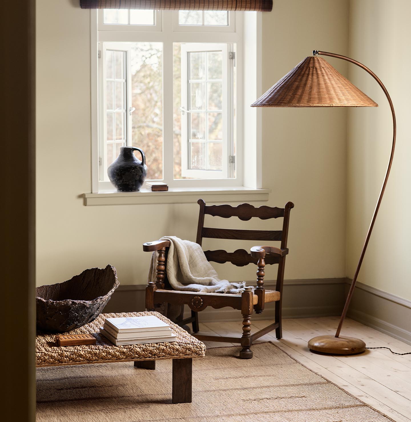 A wooden chair, woven lamp, and coffee table against a muted yellow wall painted in the colour 12080 Soft Radiance from Jotun.