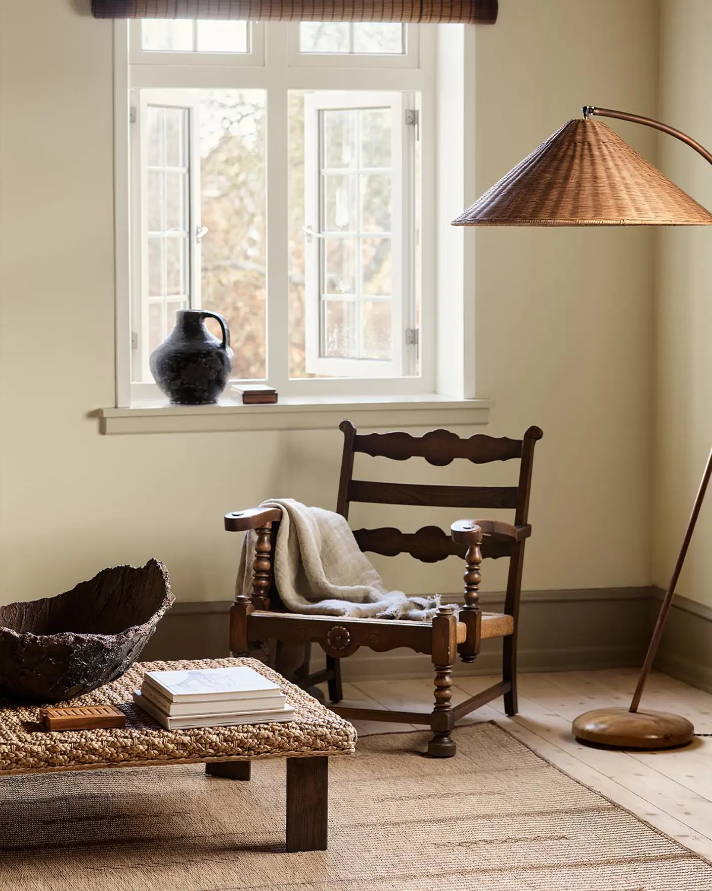 A wooden chair, woven lamp, and coffee table against a muted yellow wall painted in the colour 12080 Soft Radiance from Jotun.