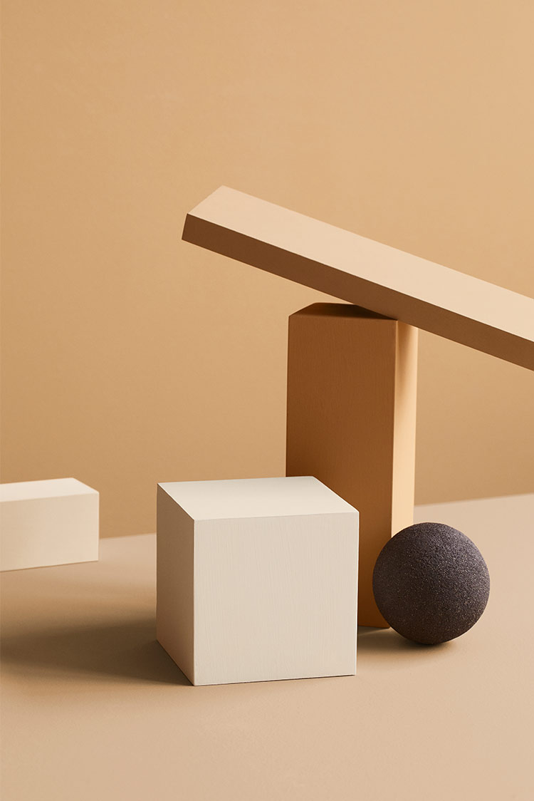 Geometriske former i minimalistisk komposisjon, inkludert en blokk, en kule og en plate, mot en okergul vegg malt i Jotun 1909 Chalk Ochre