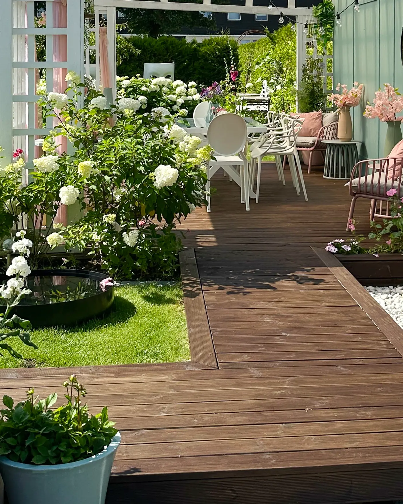 Brunt terrassegulv beiset med TREBITT Terrassebeis i Terrassebrun, ute i en grønn hage med en pergola malt hvit med JOTUN Klassisk Hvit