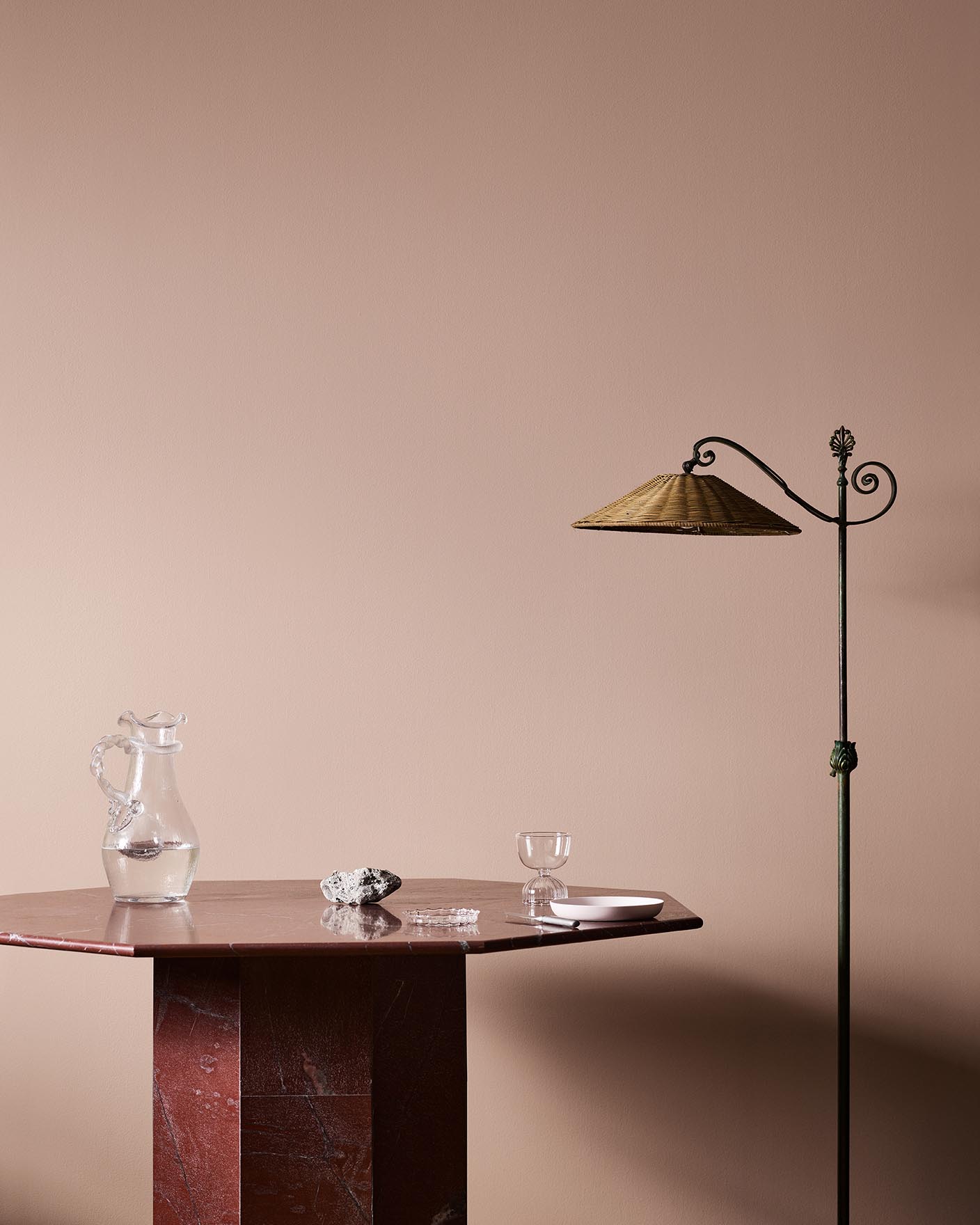 A red marble table, glassware, and floor lamp against a soft pink wall painted in the colour 20362 Pink Ambience from Jotun. 