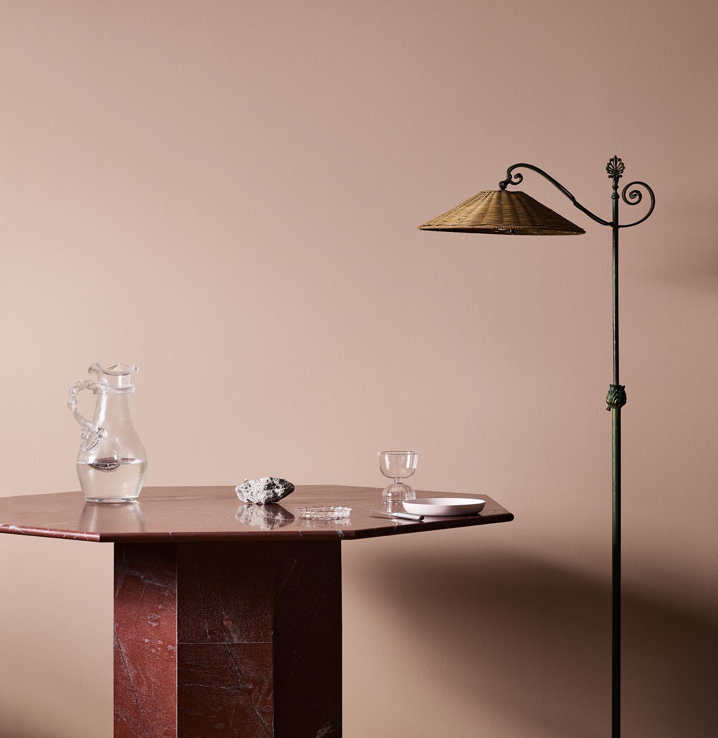 A red marble table, glassware, and floor lamp against a soft pink wall painted in the colour 20362 Pink Ambience from Jotun. 