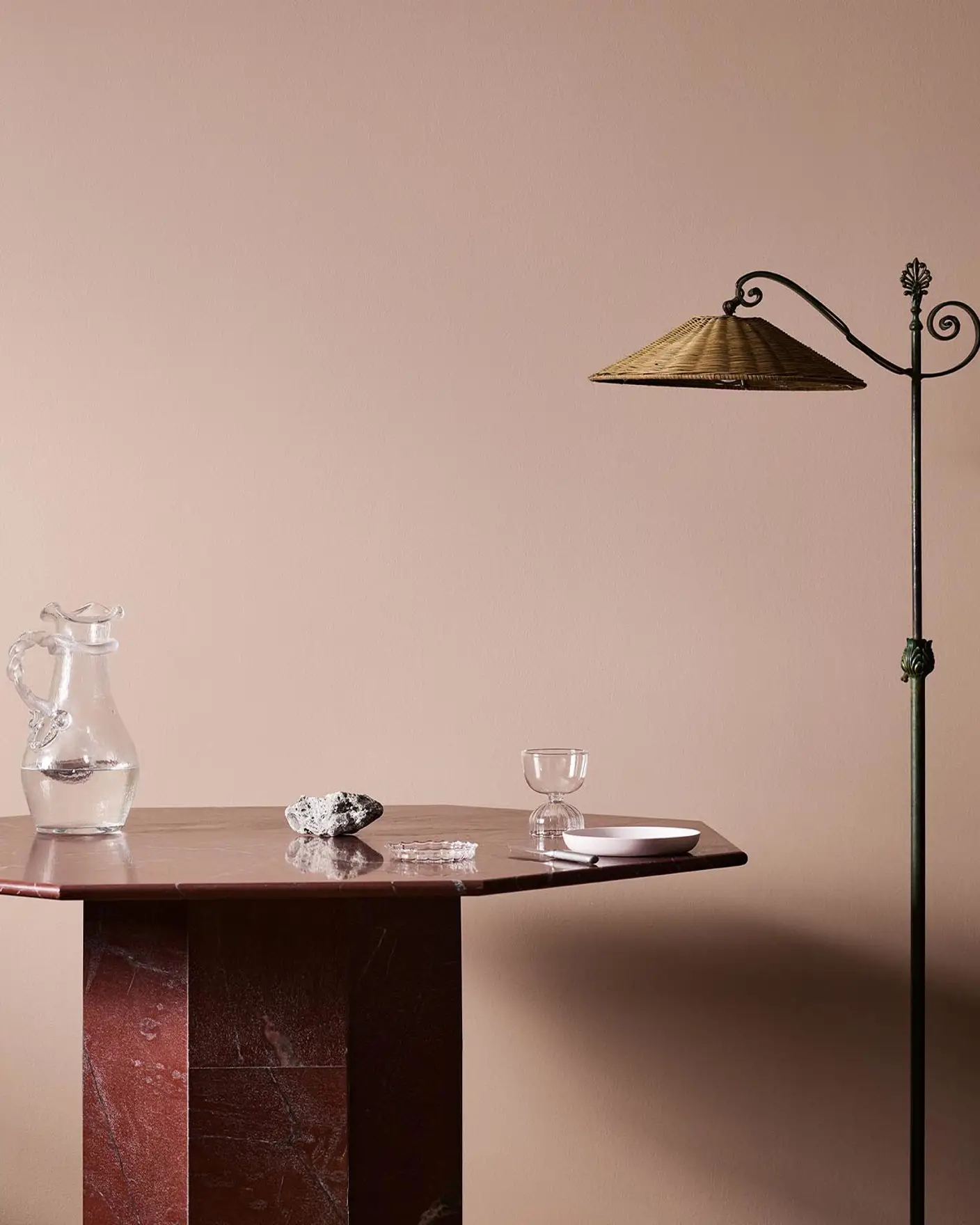A red marble table, glassware, and floor lamp against a soft pink wall painted in the colour 20362 Pink Ambience from Jotun.