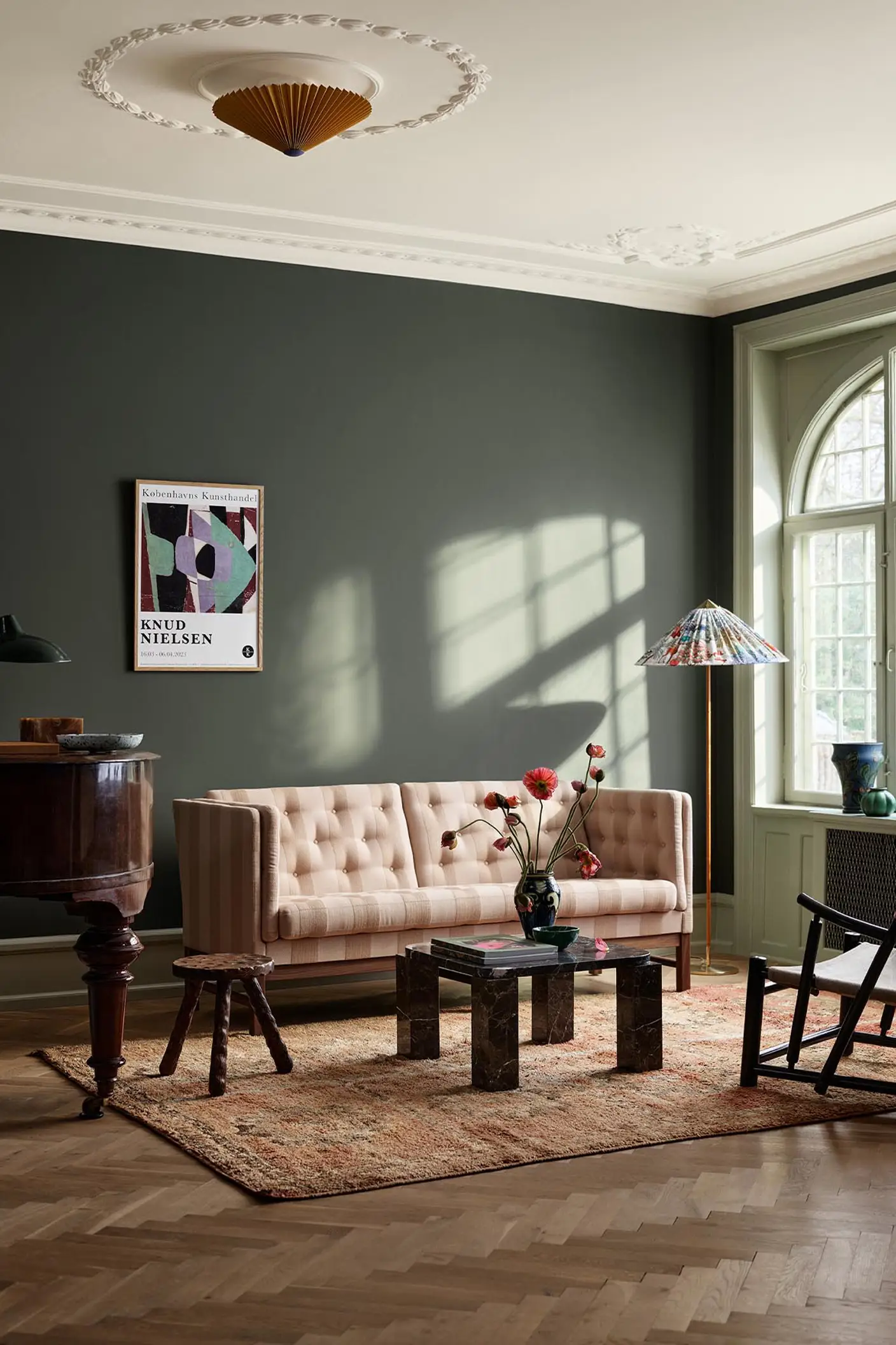 Living room with beige sofa, wooden table, and decor against a dark, muted green wall painted with the colour Jotun 7613 Northern Mystic.