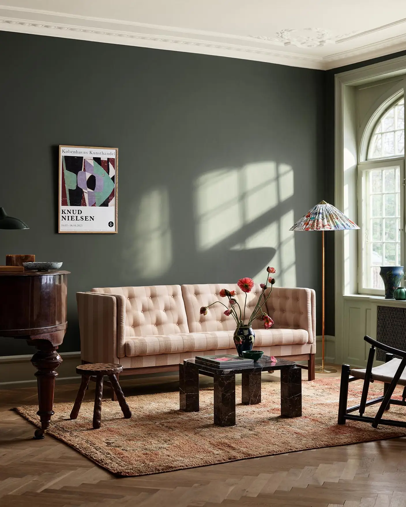 Living room with beige sofa, wooden table, and decor against a dark, muted green wall painted with the colour Jotun 7613 Northern Mystic.