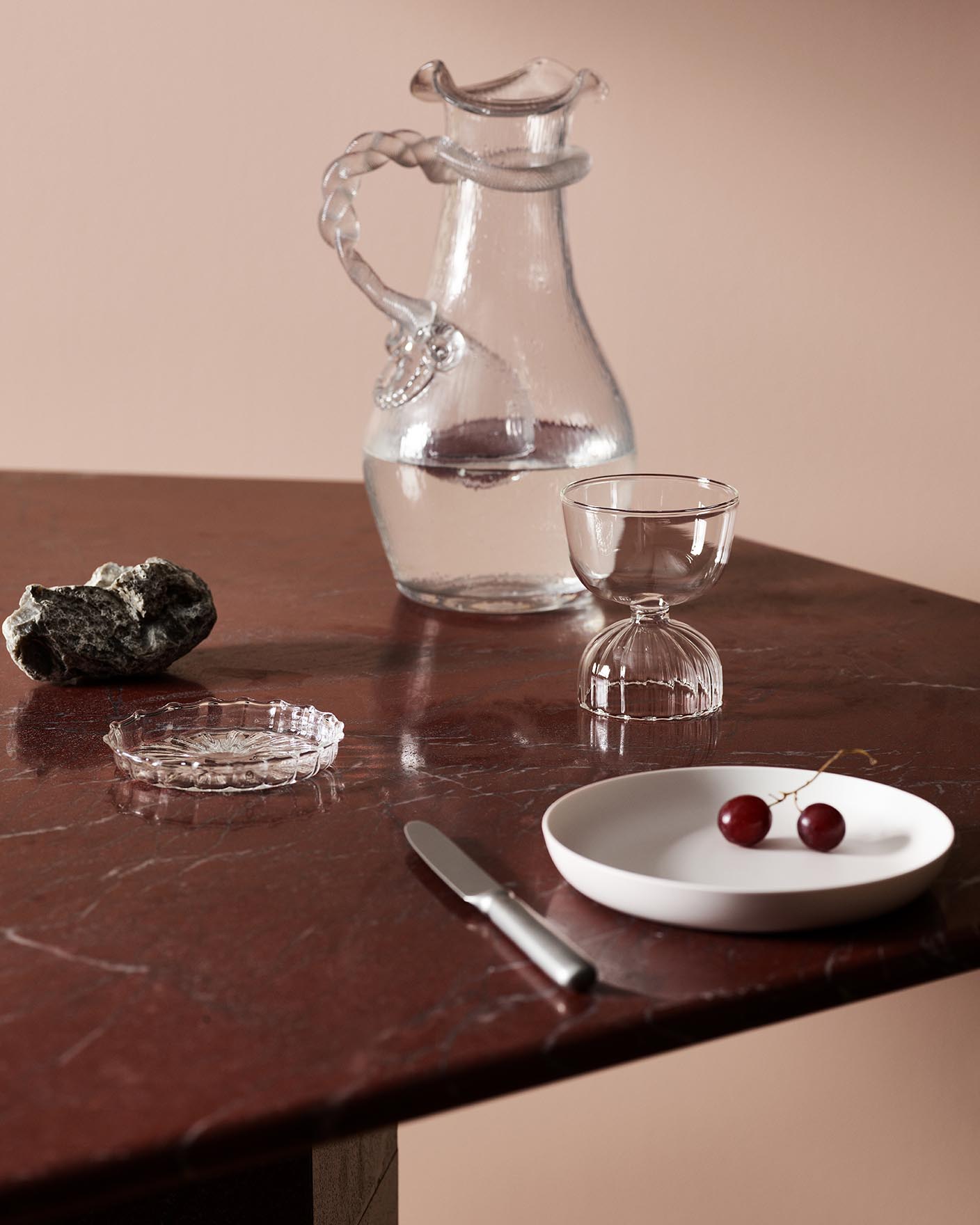 Glassware, cherries, and decor on a maroon marble table against a soft pink wall painted with the Jotun colour 20362 Pink Ambience.