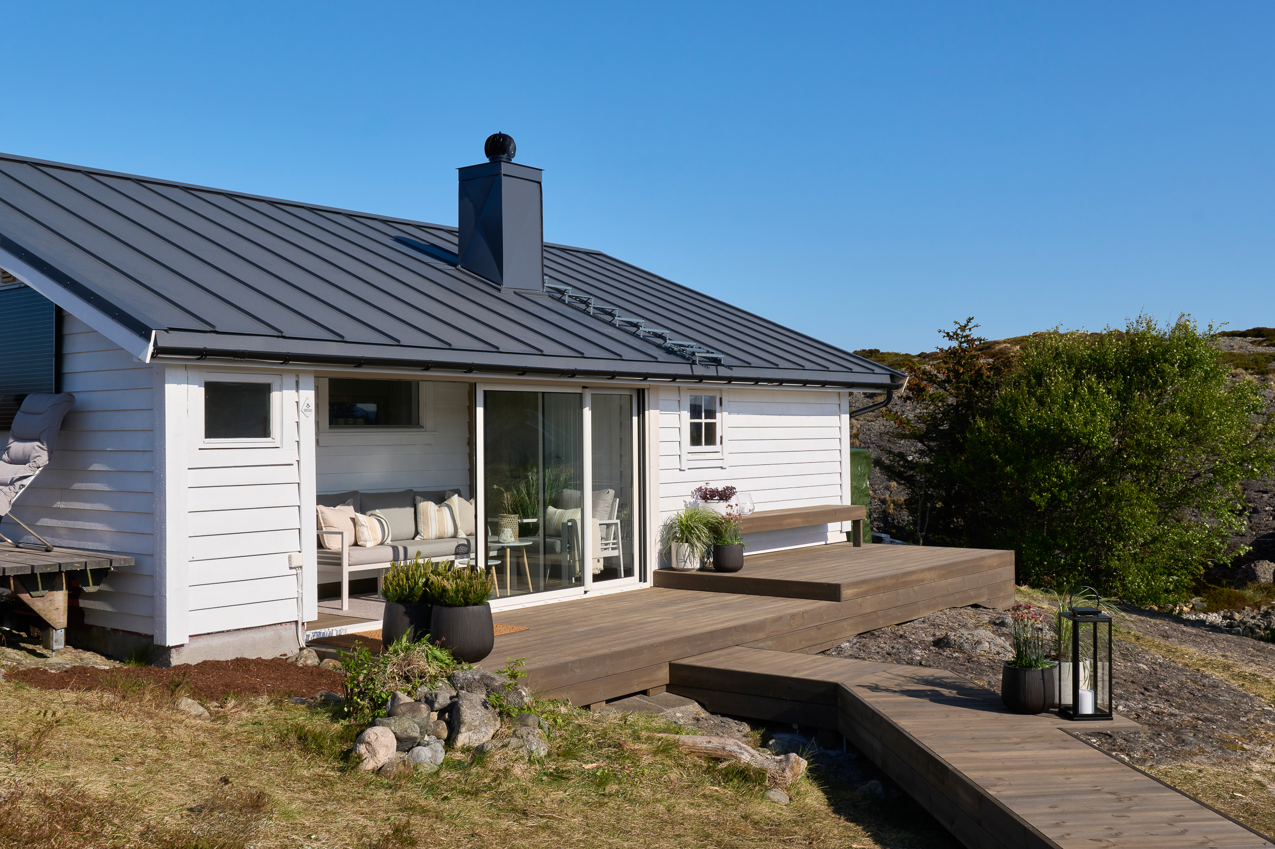 Hvit hytte med moderne design og terrasse, omgitt av natur og blå himmel, ideell for sommerferie i Norge