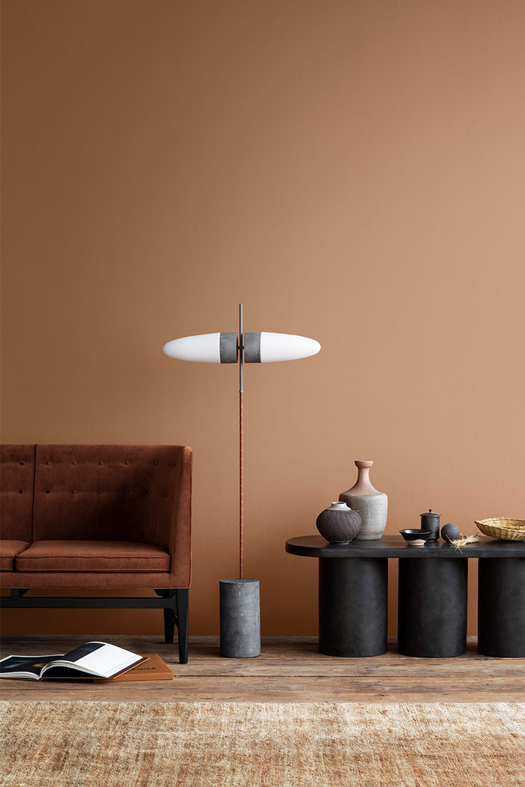 Moderne stueinteriør med en brun sofa, unik gulvlampe og dekorativ keramikk på et svart bord mot en dempet brun vegg malt i Jotun 1259 Rusty