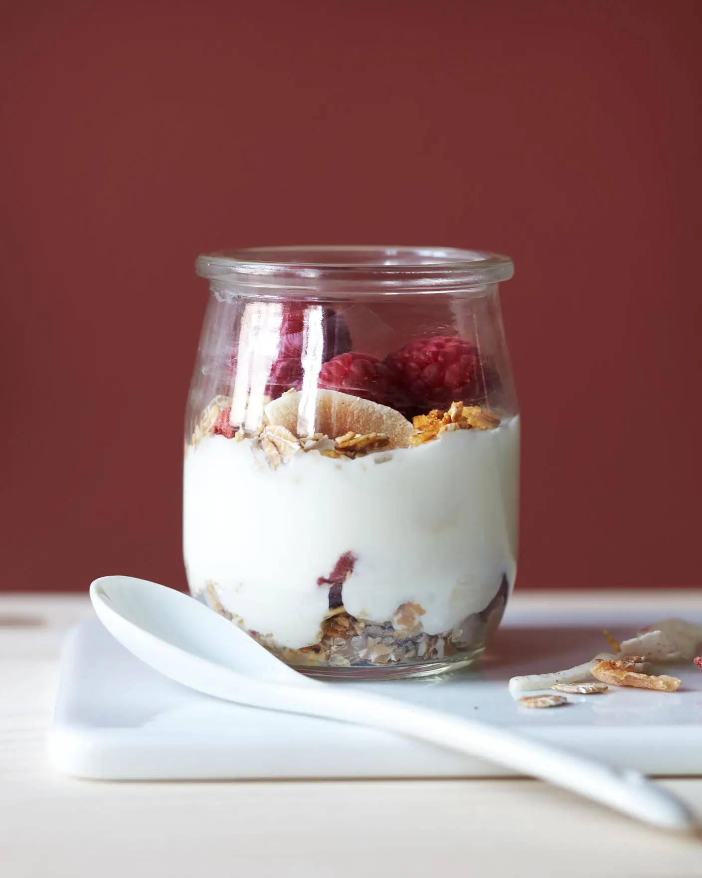 Una pared roja intensa pintada con Jotun 2859 Whispering Red aporta calidez y profundidad a un desayuno sencillo con yogur, granola y frutos rojos.