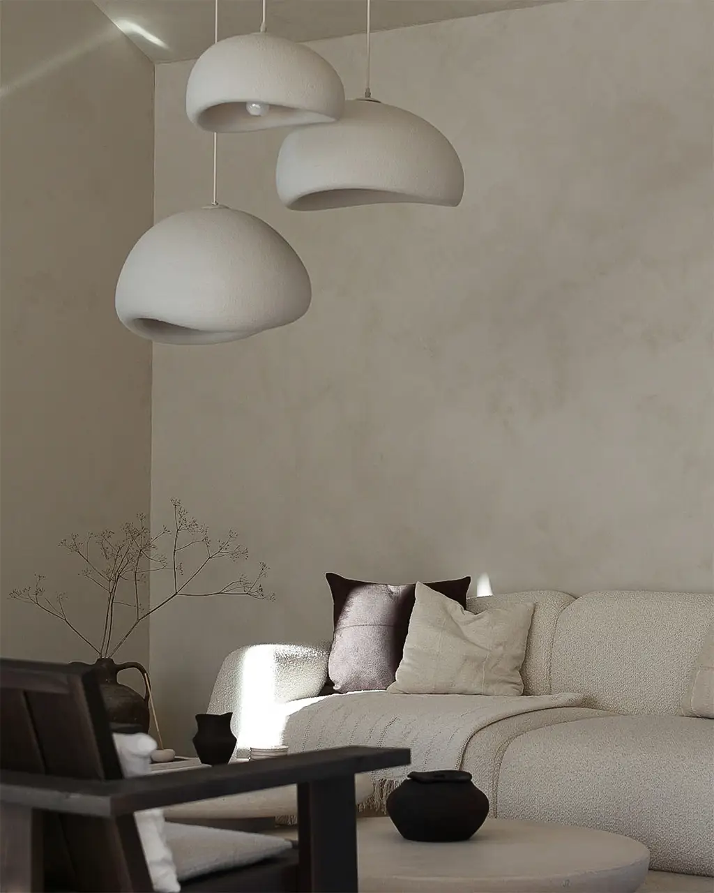Lyst stuehjørne med beige sofa, mørke puter og organiske lamper i hvitt mot en kalkmalt vegg malt i fargen Jotun Sand