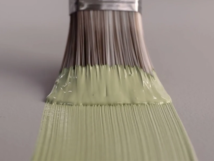 Pensel med lys grønn maling stryker malingen utover en grålilla flate