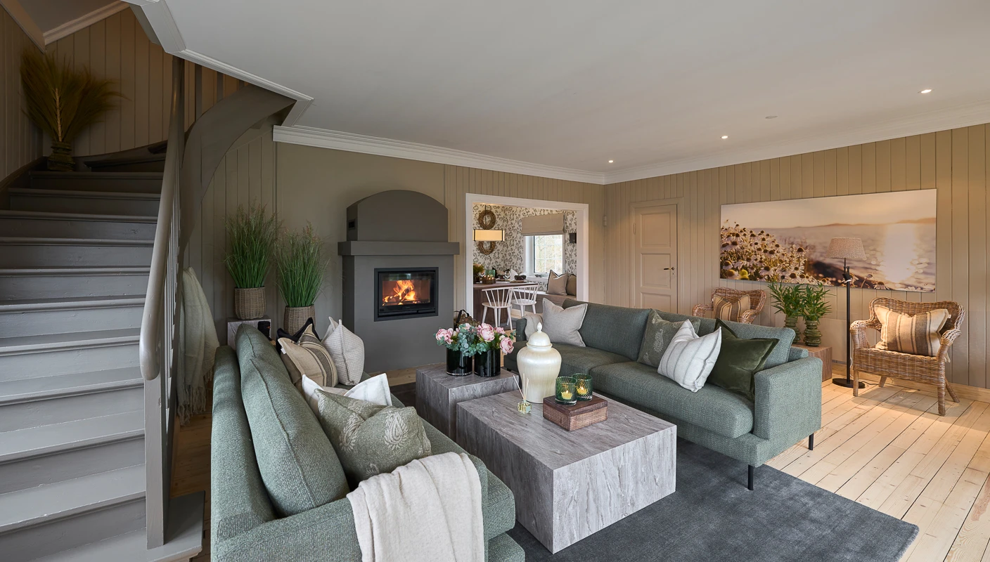 Hyttestue med grønne sofaer, stort ildsted og lun stemning, beige vegger malt i Jotun LADY Sandbeige.