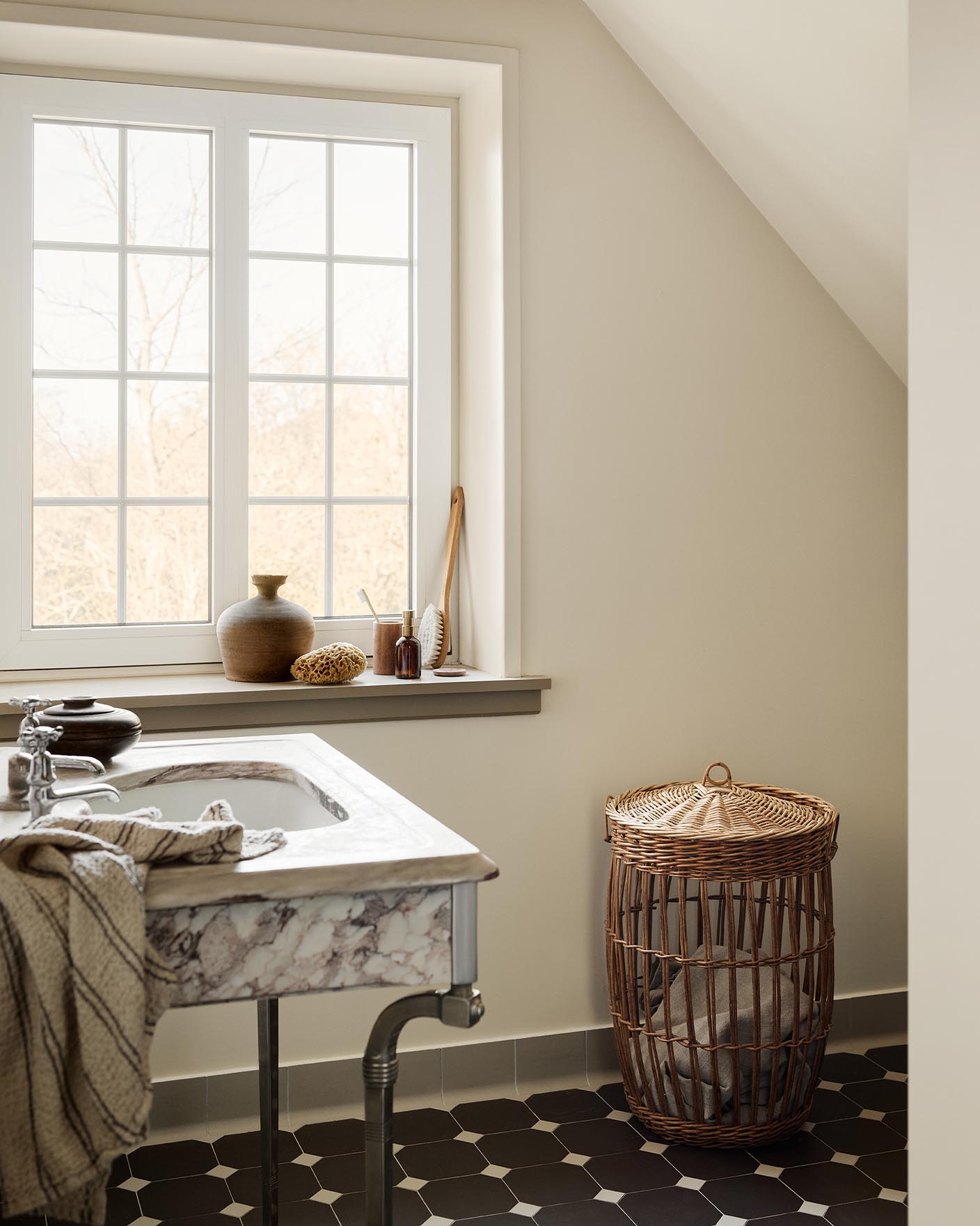 Bathroom with a marble sink, patterned floor tiles, and a wicker laundry basket against a wall painted with 12079 Gleam - a muted, greenish yellow colour from Jotun.