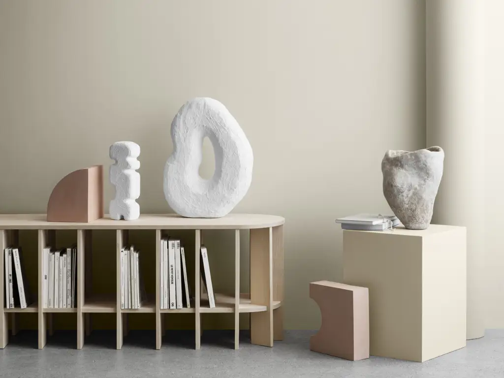 Minimalistisk interiør med skulpturelle dekorobjekter i naturmaterialer og lyse toner. Veggen er malt i en varm, beige nyanse som gir et rolig og harmonisk uttrykk, perfekt nøytral for moderne stue.