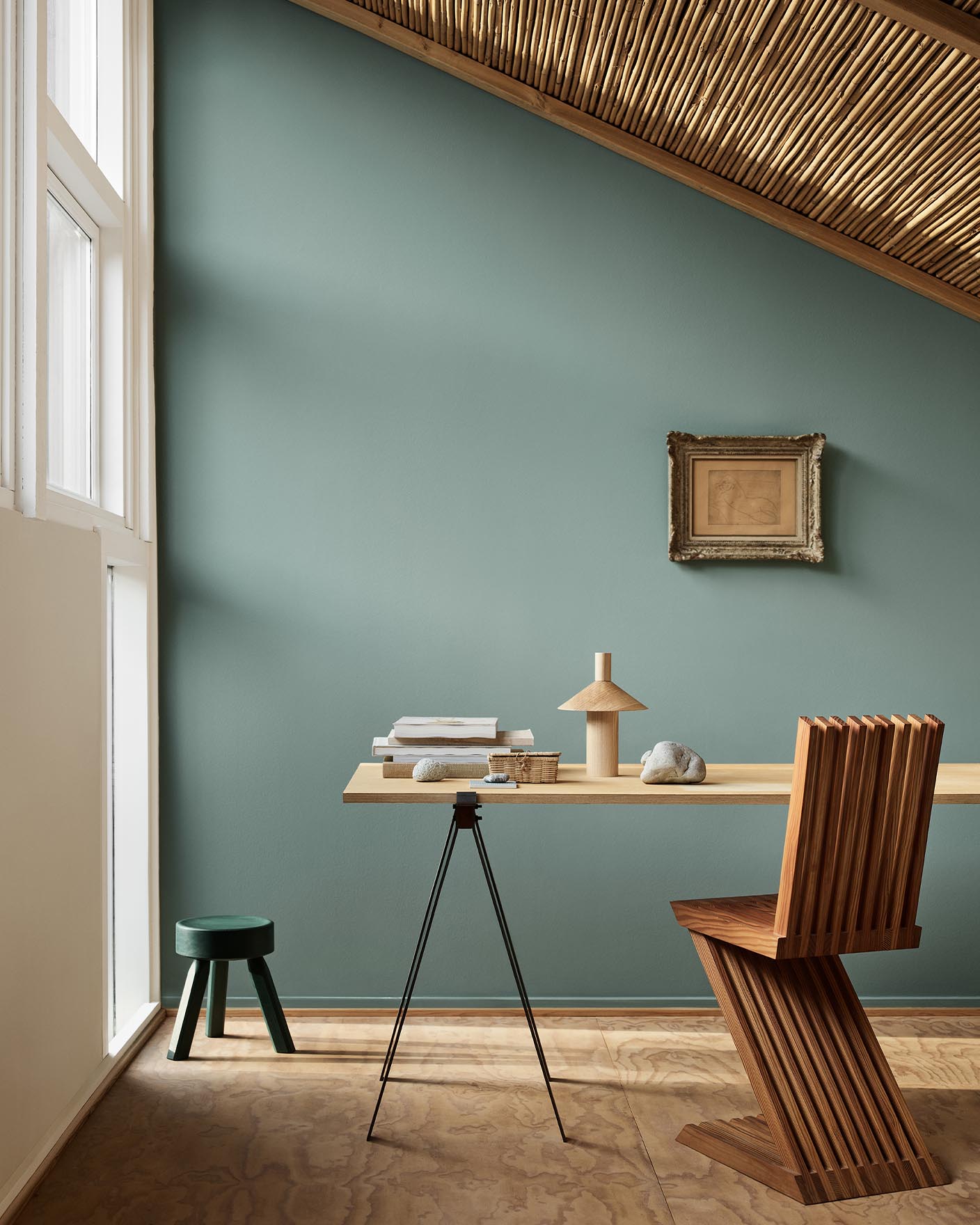 Minimalist workspace with wooden desk and decor against a muted bluish green wall in the colour 6379 Cityscape from Jotun.