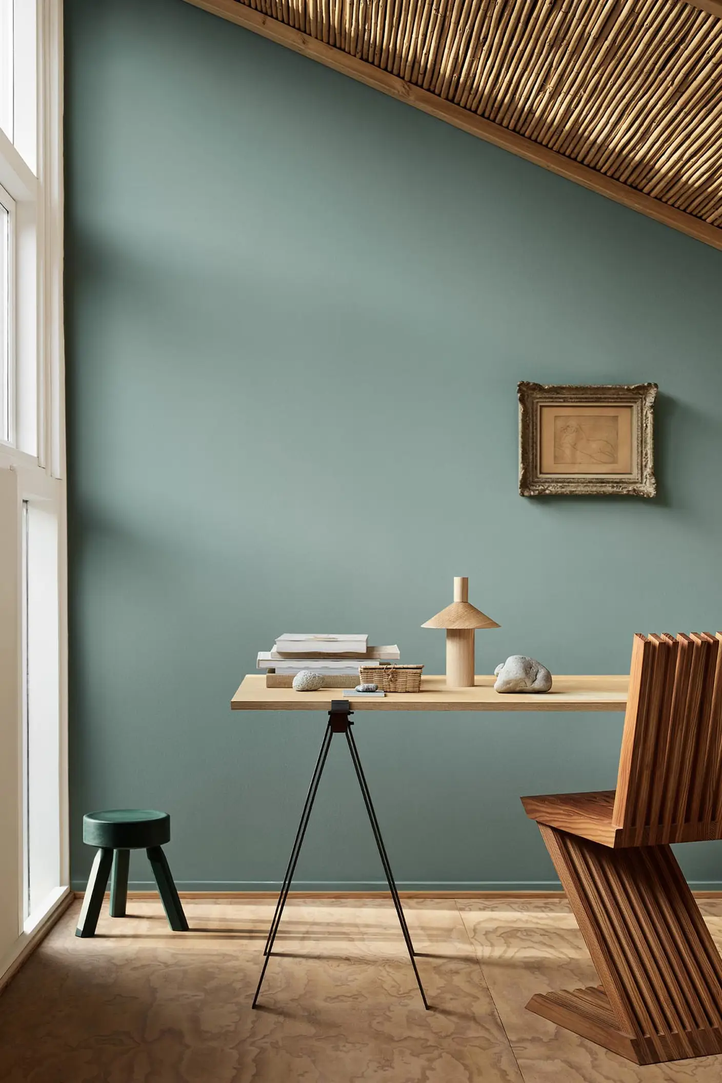 Minimalist workspace with wooden desk and decor against a muted bluish green wall in the colour 6379 Cityscape from Jotun.