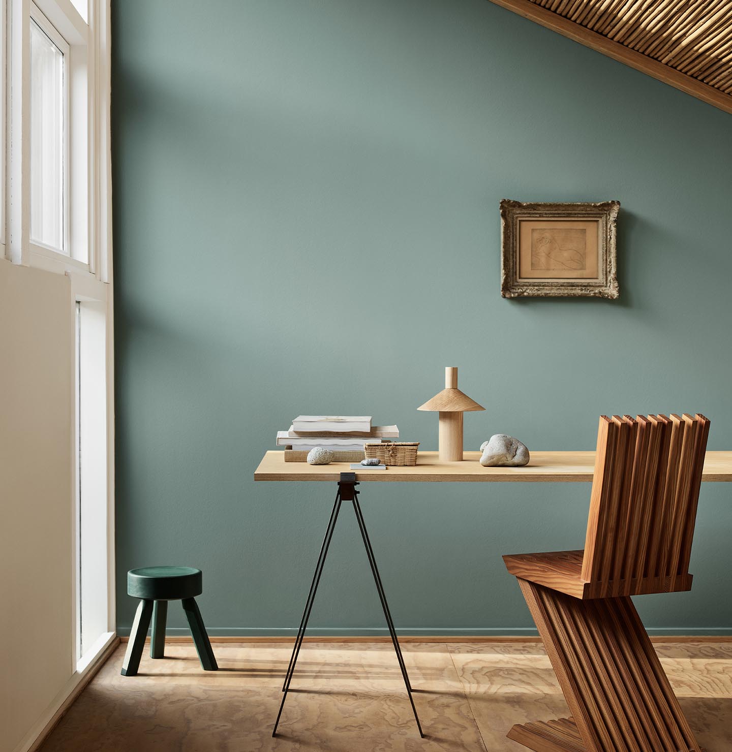 Minimalist workspace with wooden desk and decor against a muted bluish green wall in the colour 6379 Cityscape from Jotun.
