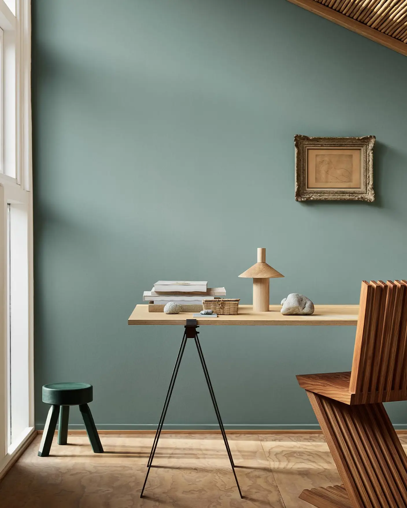 Minimalist workspace with wooden desk and decor against a muted bluish green wall in the colour 6379 Cityscape from Jotun.