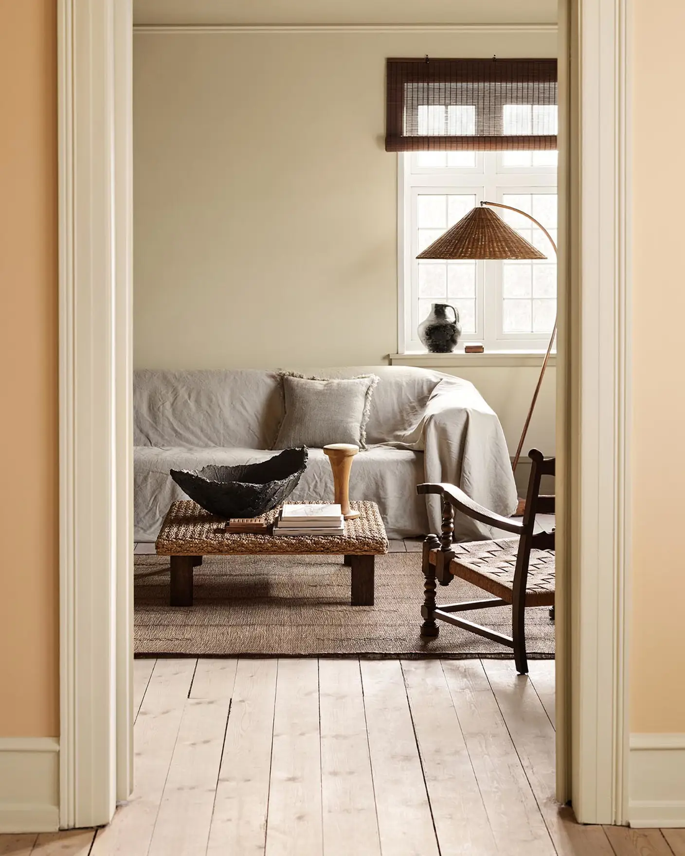 Living room with a light sofa, woven coffee table against a muted yellow wall painted in 12080 Soft Radiance. Wall in front in the colour 11202 Mild Ochre.