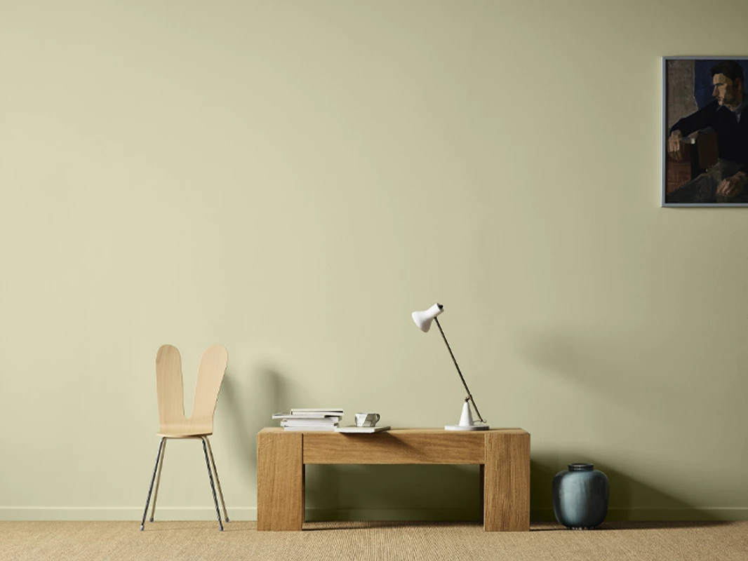 Trebord og stol mot en lysegrønn vegg malt i Jotun Sunny Green