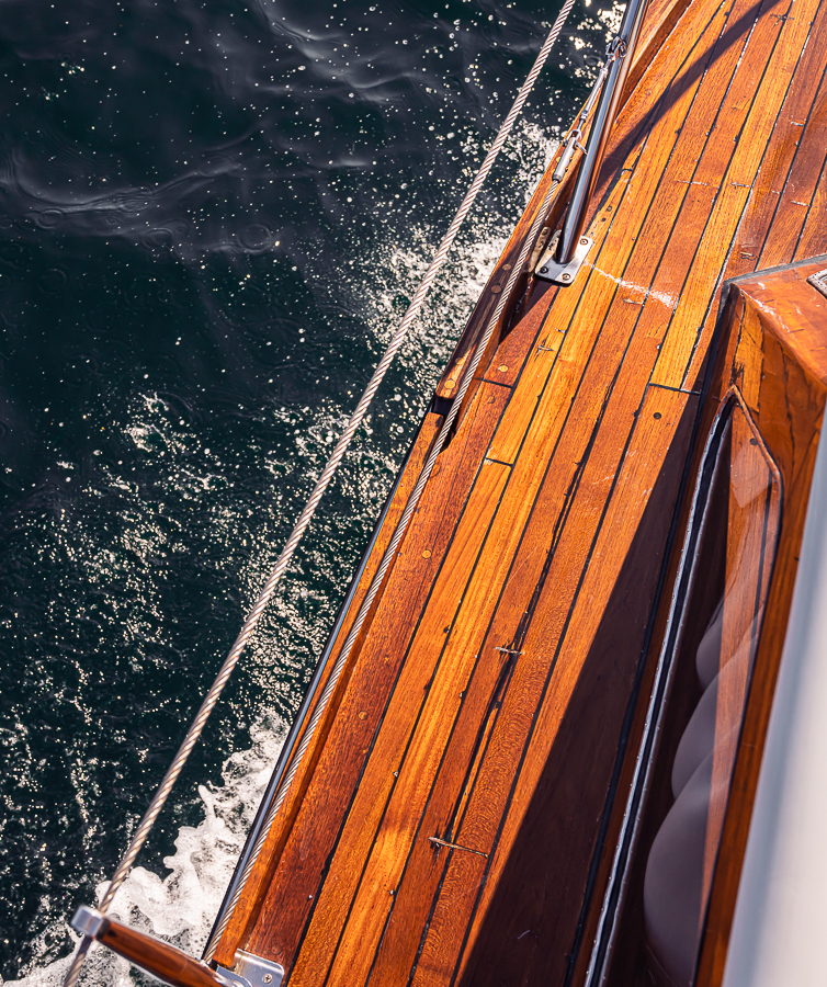 Utsnitt av siden på en blank trebåt sett ovenfra, som skjærer gjennom vannet.