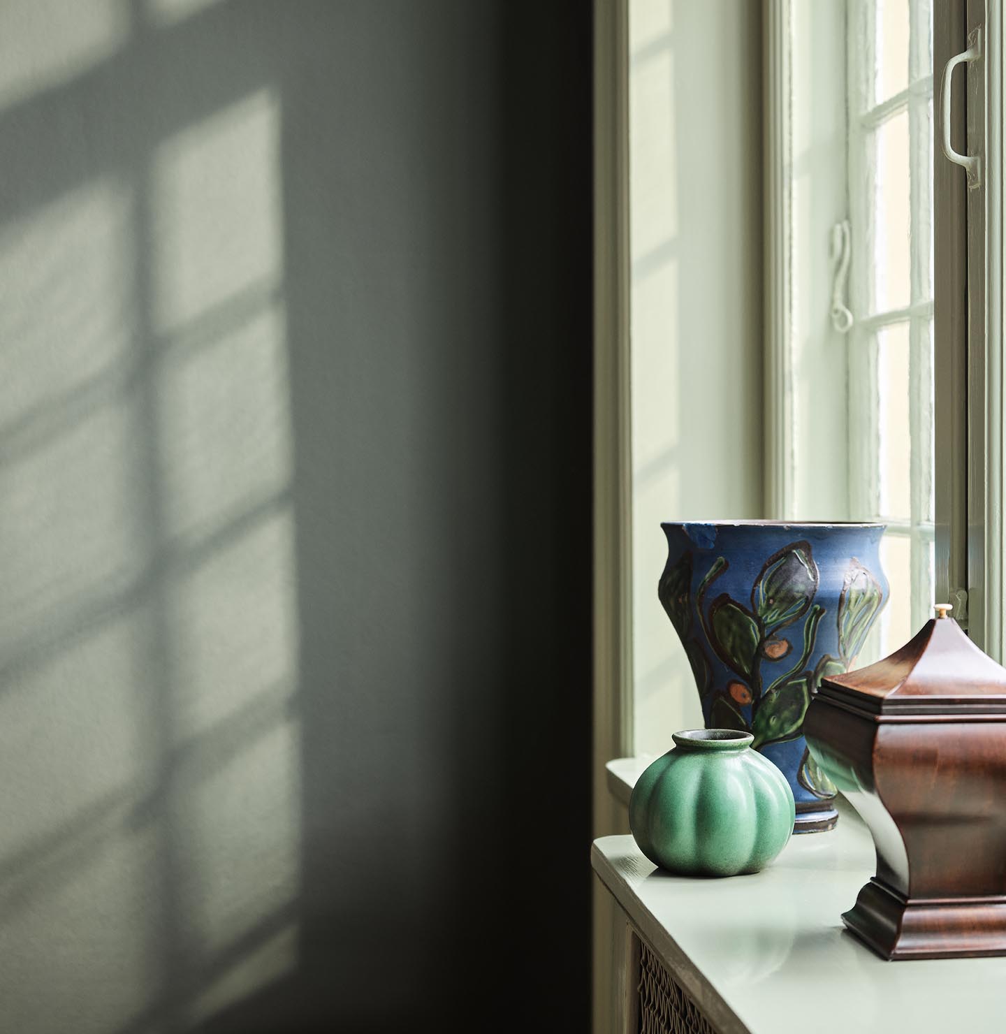 Green and blue vases standing in a window against a muted, dark green wall painted with the colour 7613 Northern Mystic from Jotun.