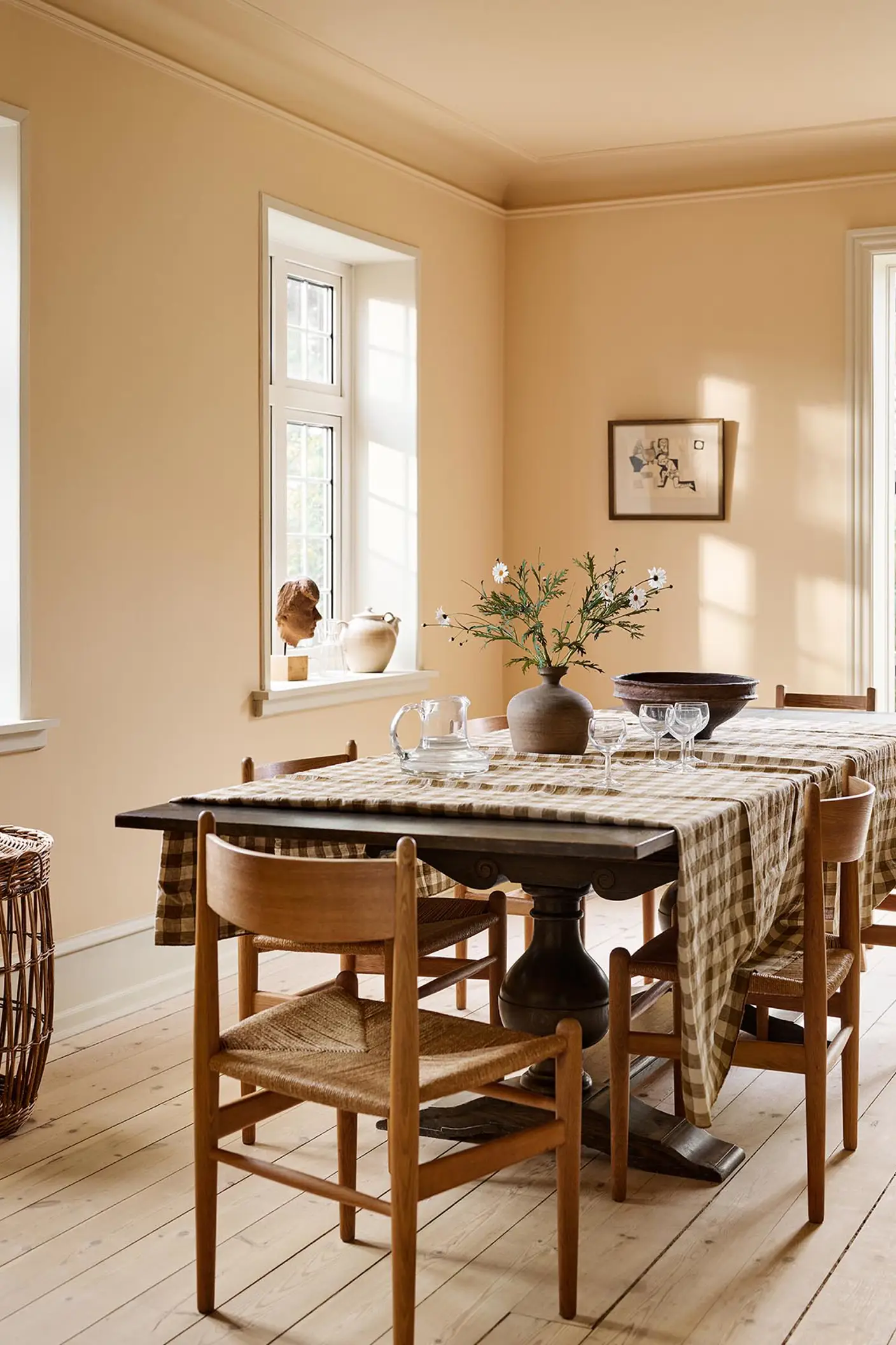 Dining room with a checkered tablecloth, wooden chairs, against an ochre yellow wall painted in the colour 11202 Mild Ochre from Jotun.