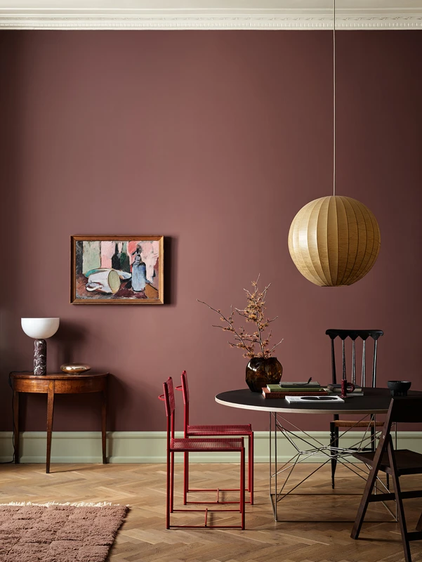 Moderne stue med burgunderrød vegg malt i Jotun 2951 Sophisticated Red, rundt spisebord med svarte og røde stoler, hengelampe i kurv, og kunstverk på veggen