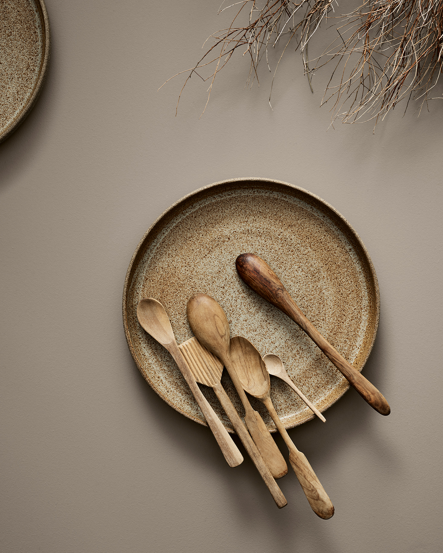 Rustik tallrik med olika träslevar och köksredskap mot en neutral bakgrund. Bordsytan är målad i Jotun 11130 Shade.