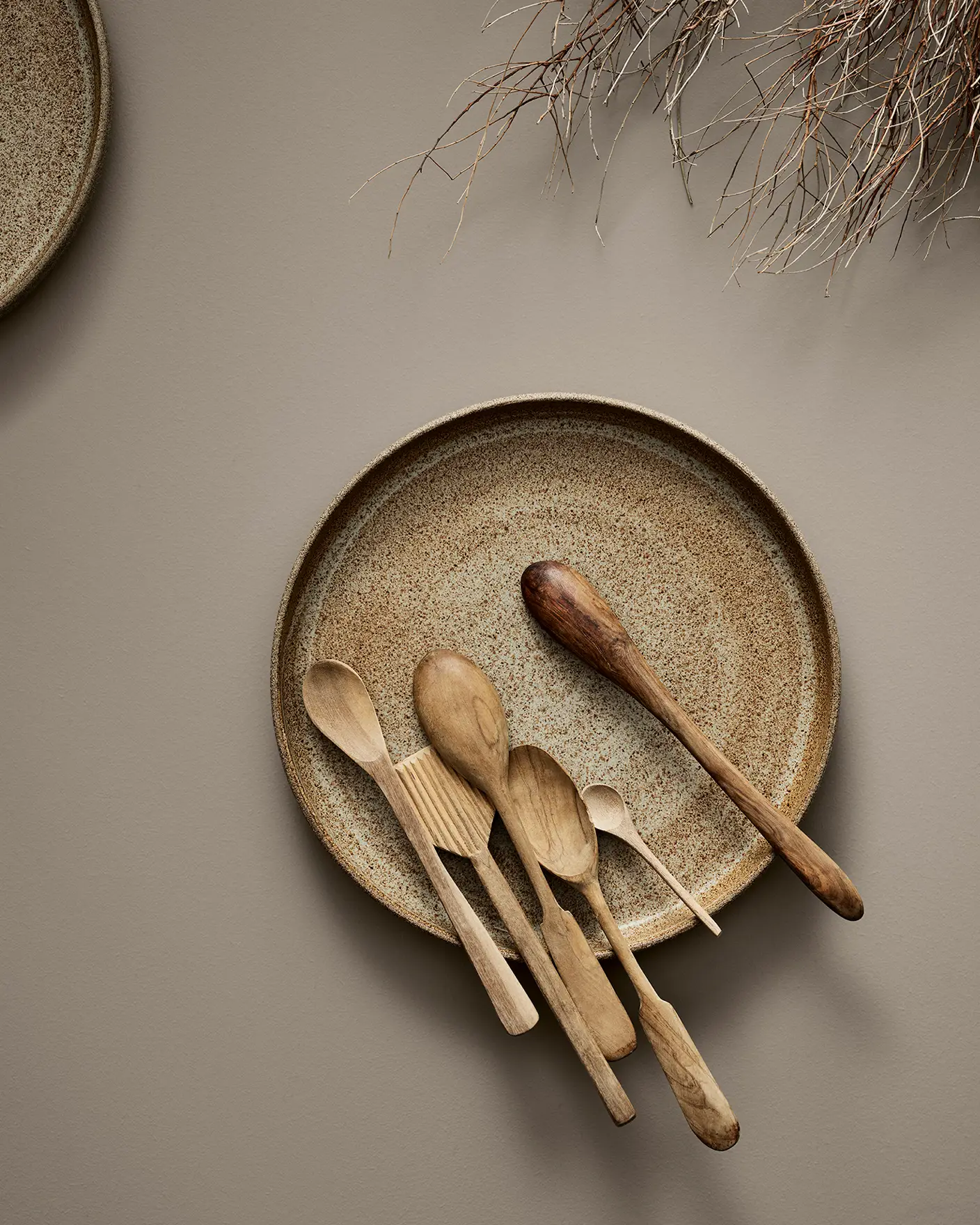 Rustik tallrik med olika träslevar och köksredskap mot en neutral bakgrund. Bordsytan är målad i Jotun 11130 Shade.
