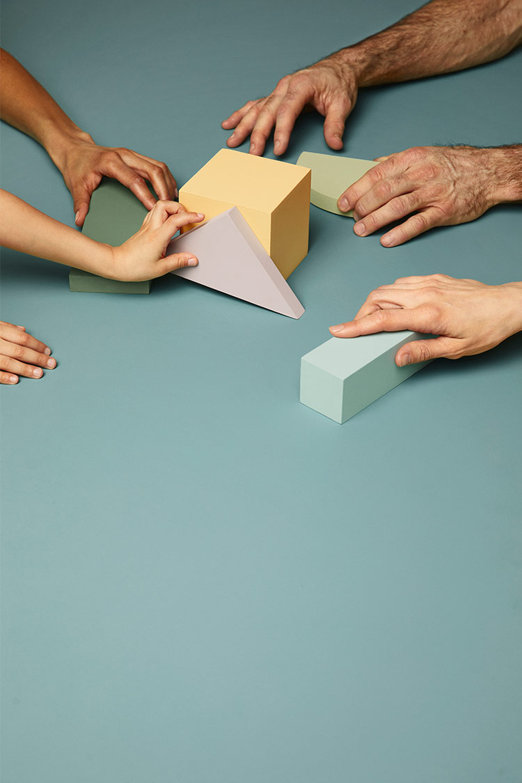 Flere hender organiserer ulike geometriske byggeklosser på et turkist bord malt i Jotun 6284 Wish