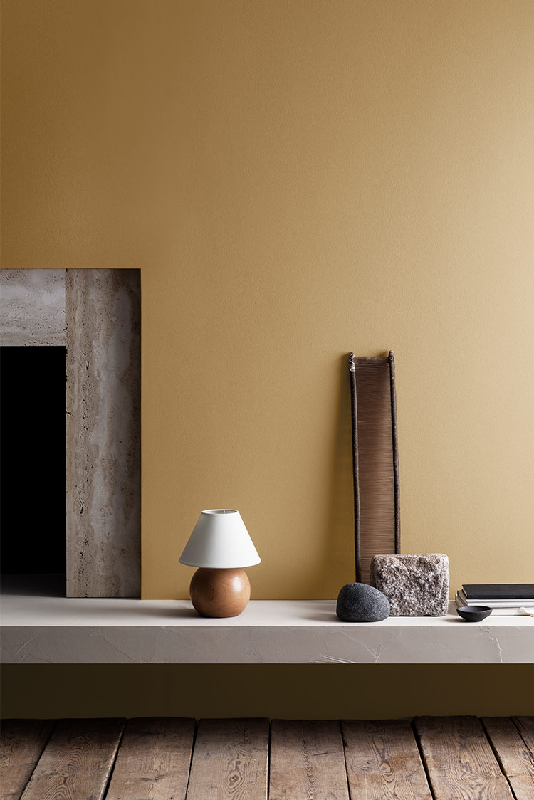 Minimalistisk interiørdesign med naturlige elementer, med tregulv, steininnslag, okergul vegg malt i Jotun 19091 Chalk Ochre, moderne lampe og dekorative gjenstander på en hylle