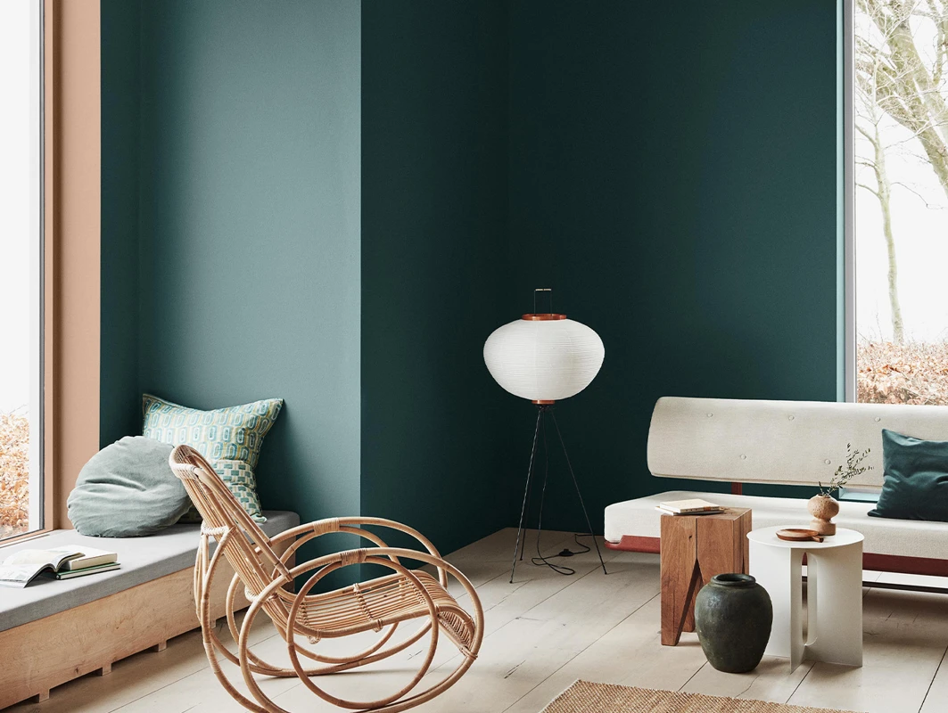 Contemporary living room with walls in Jotun 5489 Free Spirit, light wood flooring, rattan chair, minimalist bench, and neutral décor.