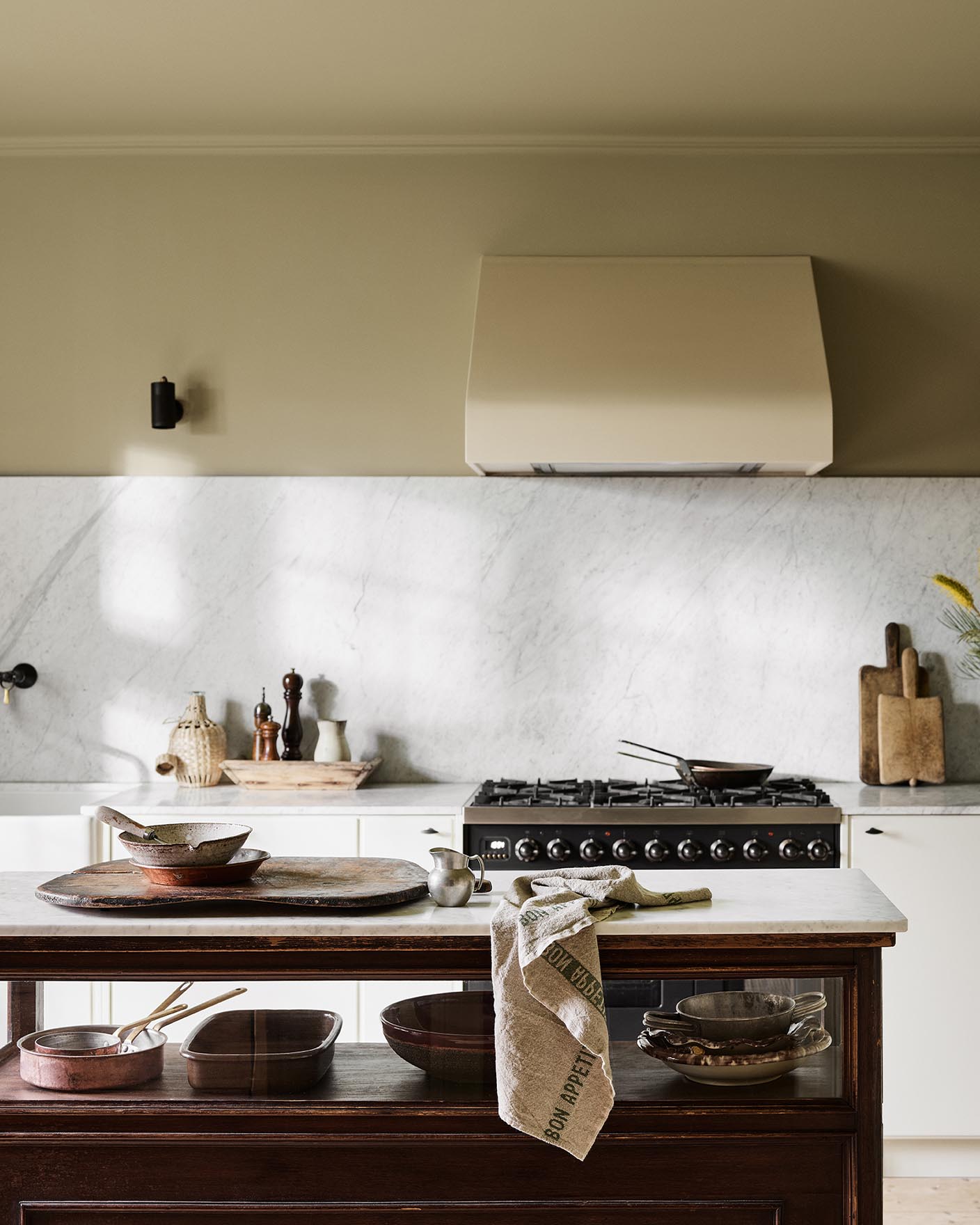 Kitchen with a marble backsplash, white cabinets, and a wooden island. Wall painted with the Jotun colour  8284 Olive.