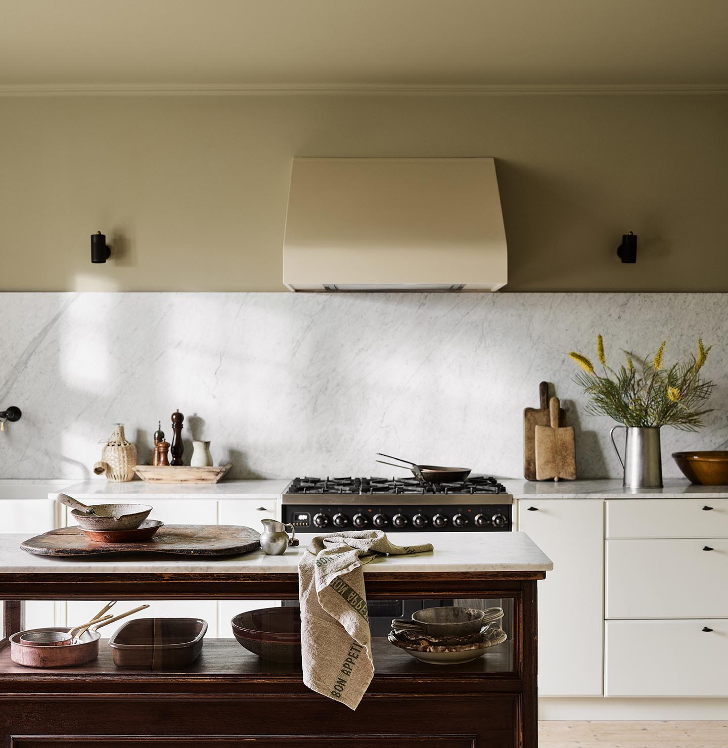 Kitchen with a marble backsplash, white cabinets, and a wooden island. Wall painted with the Jotun colour  8284 Olive.