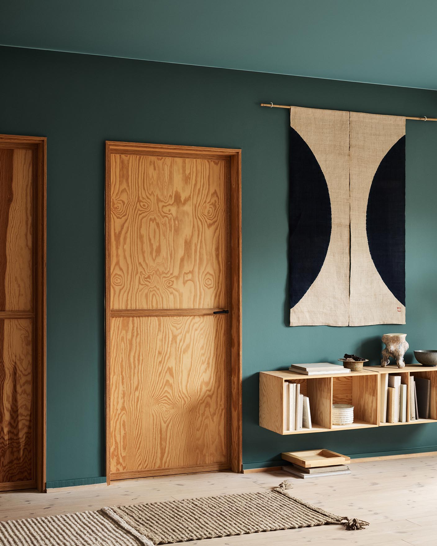 Modern interior with wooden doors, shelf, and decor against a muted, bluish green wall painted in the Jotun colour 6194 Wild Ivy.