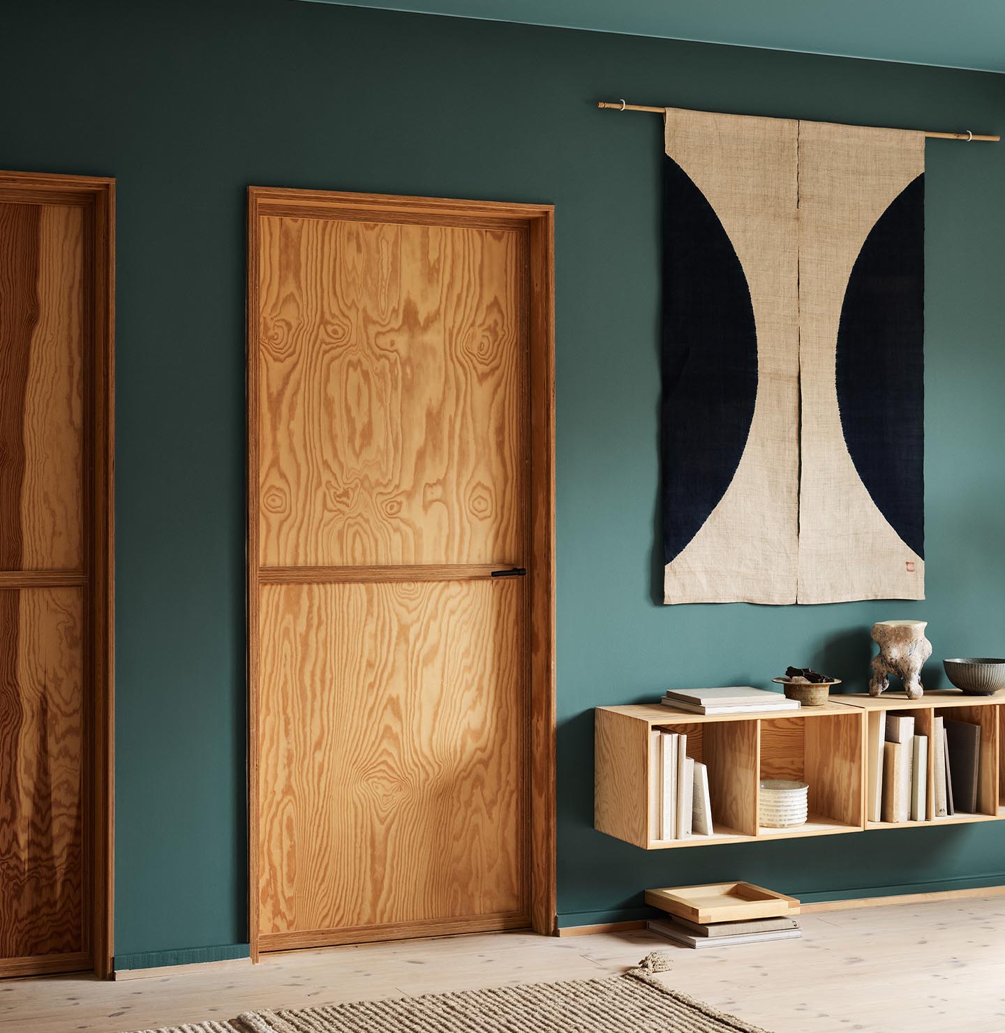 Modern interior with wooden doors, shelf, and decor against a muted, bluish green wall painted in the Jotun colour 6194 Wild Ivy.