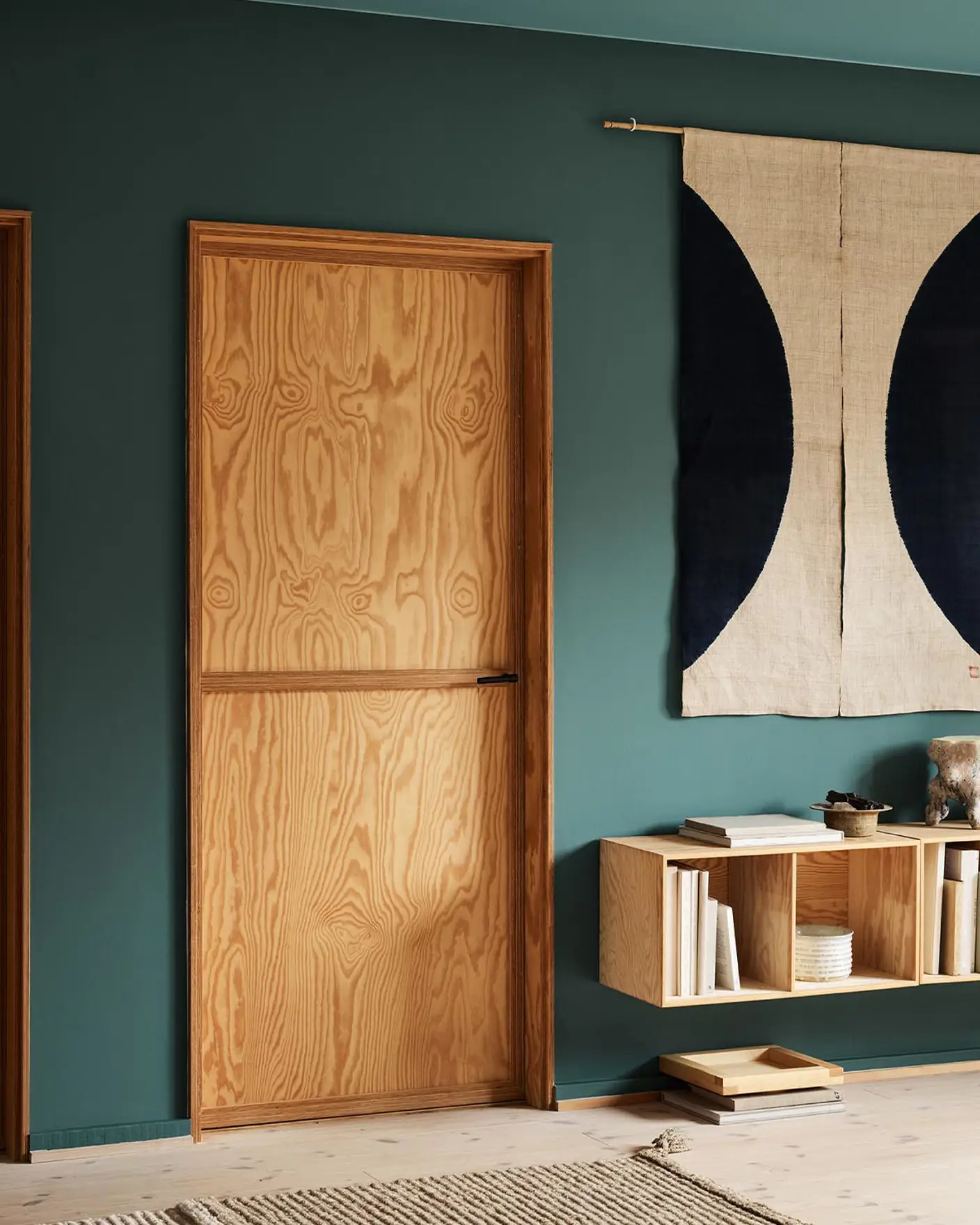 Modern interior with wooden doors, shelf, and decor against a muted, bluish green wall painted in the Jotun colour 6194 Wild Ivy.