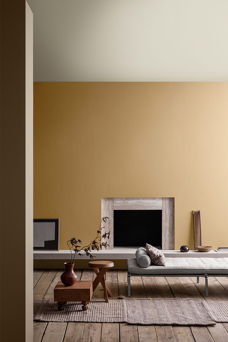 Minimalistisk stue med en beige vegg, med peis, moderne møbler, tregulv, og dekorative elementer som en vase, innrammet kunst og et vevd teppe