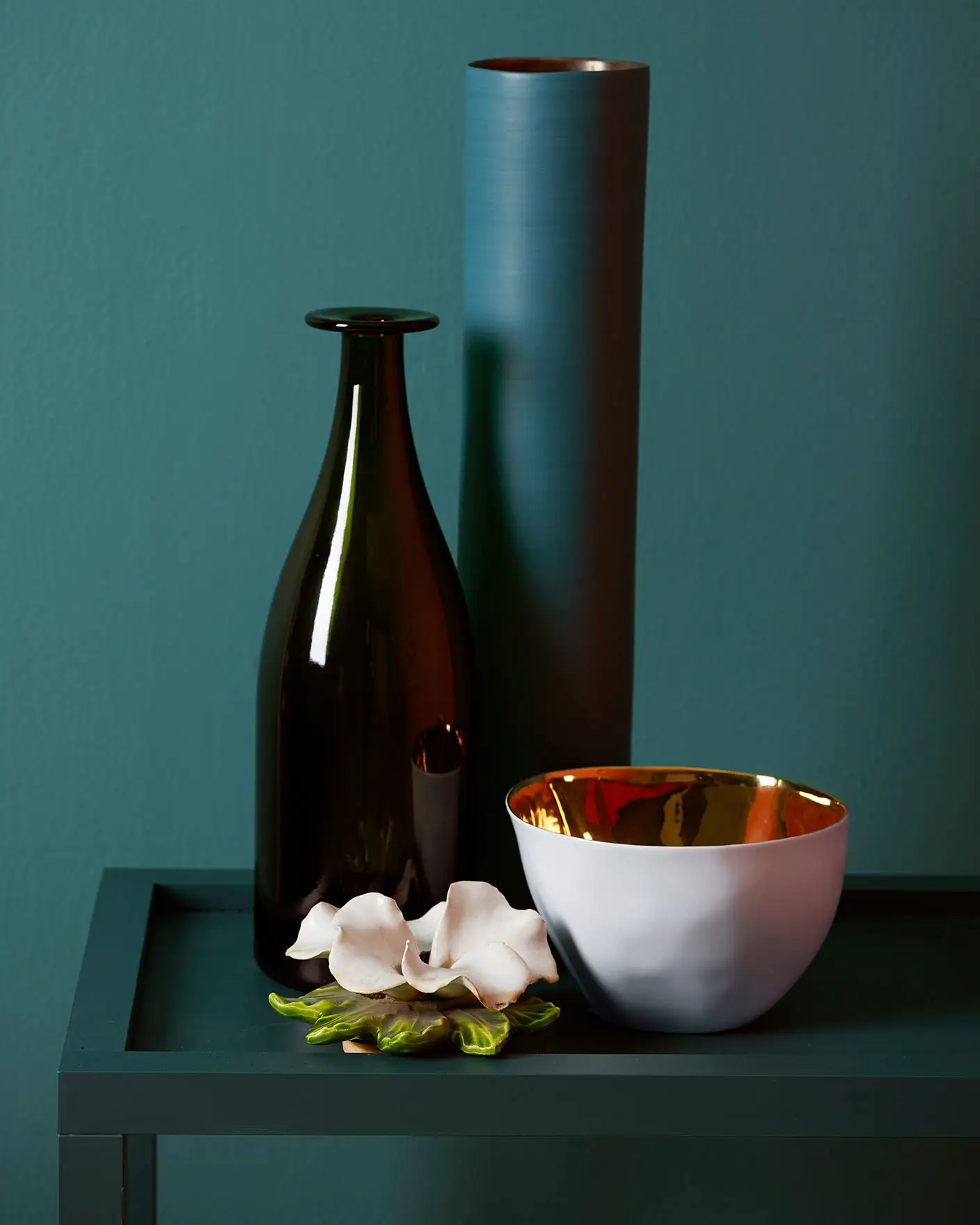 Dark green bedside table with decorations against a muted, greenish blue wall painted with Jotun 5362 Fusion.