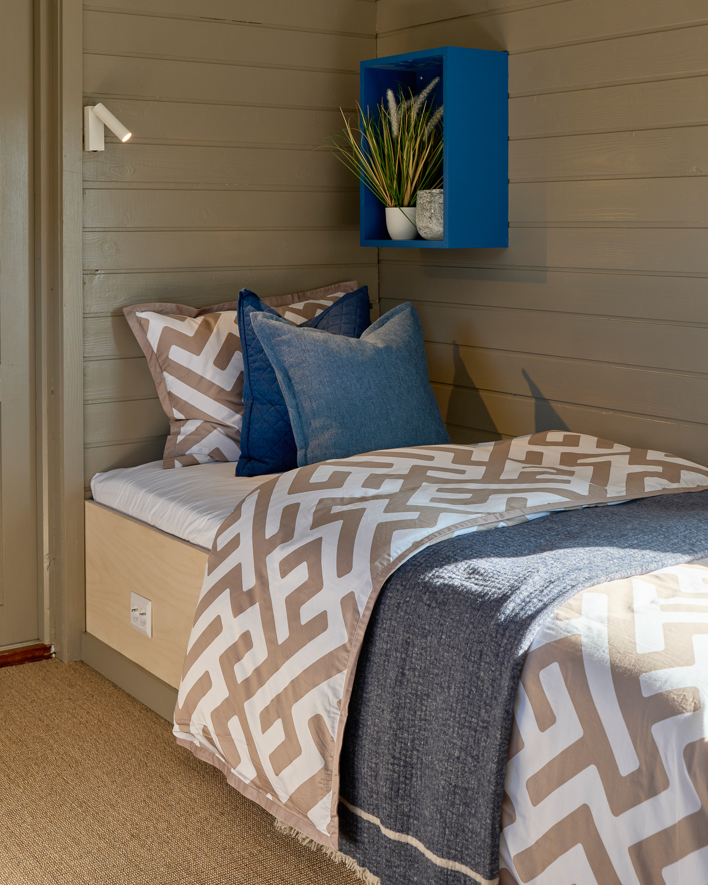 Soverom i anneks med malt trepanel og blåmalt hylle som nattbord over seng