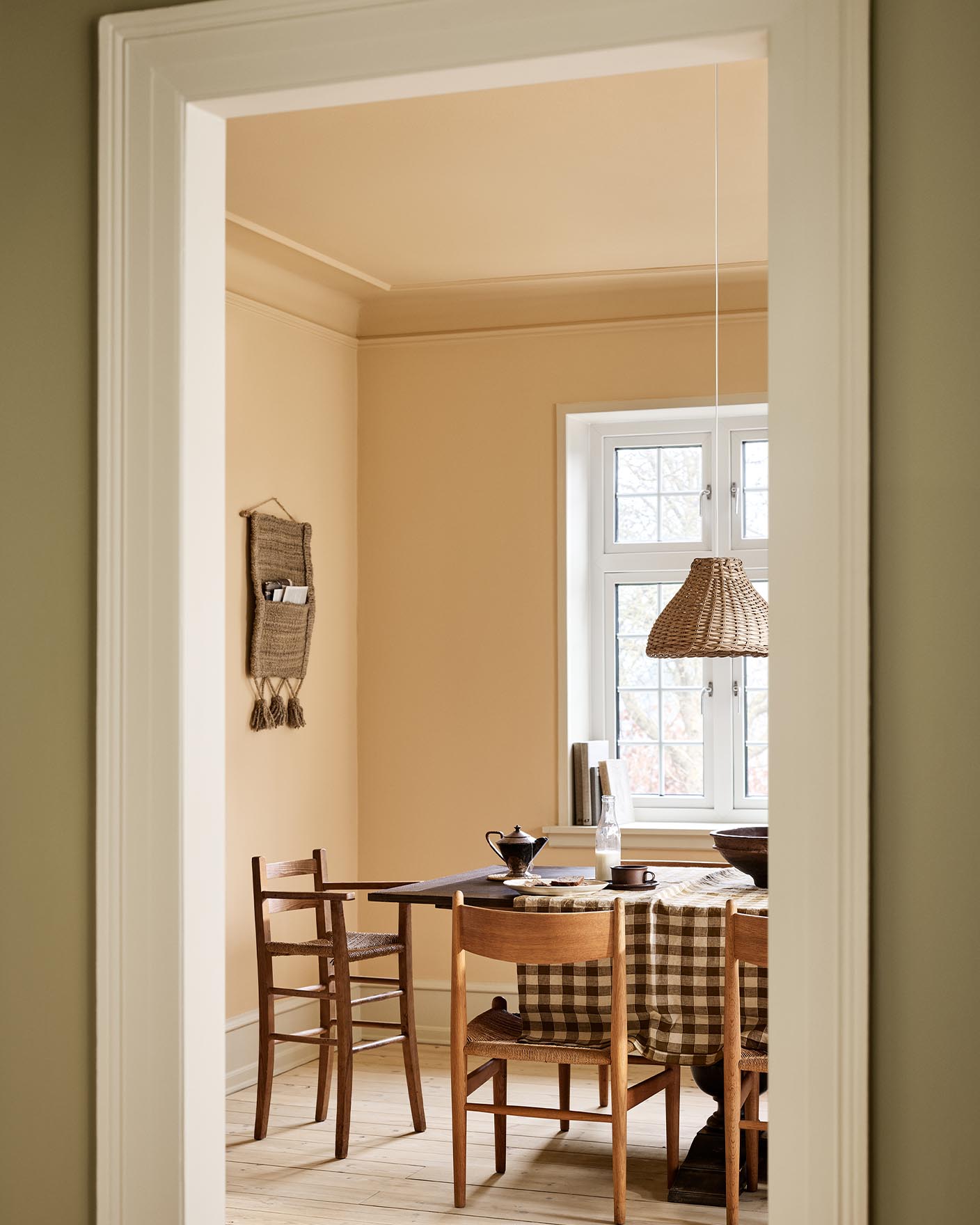 Dining area with a checkered tablecloth, wooden chairs, and ochre coloured walls and ceiling painted with Jotun's 11202 Mild Ochre.