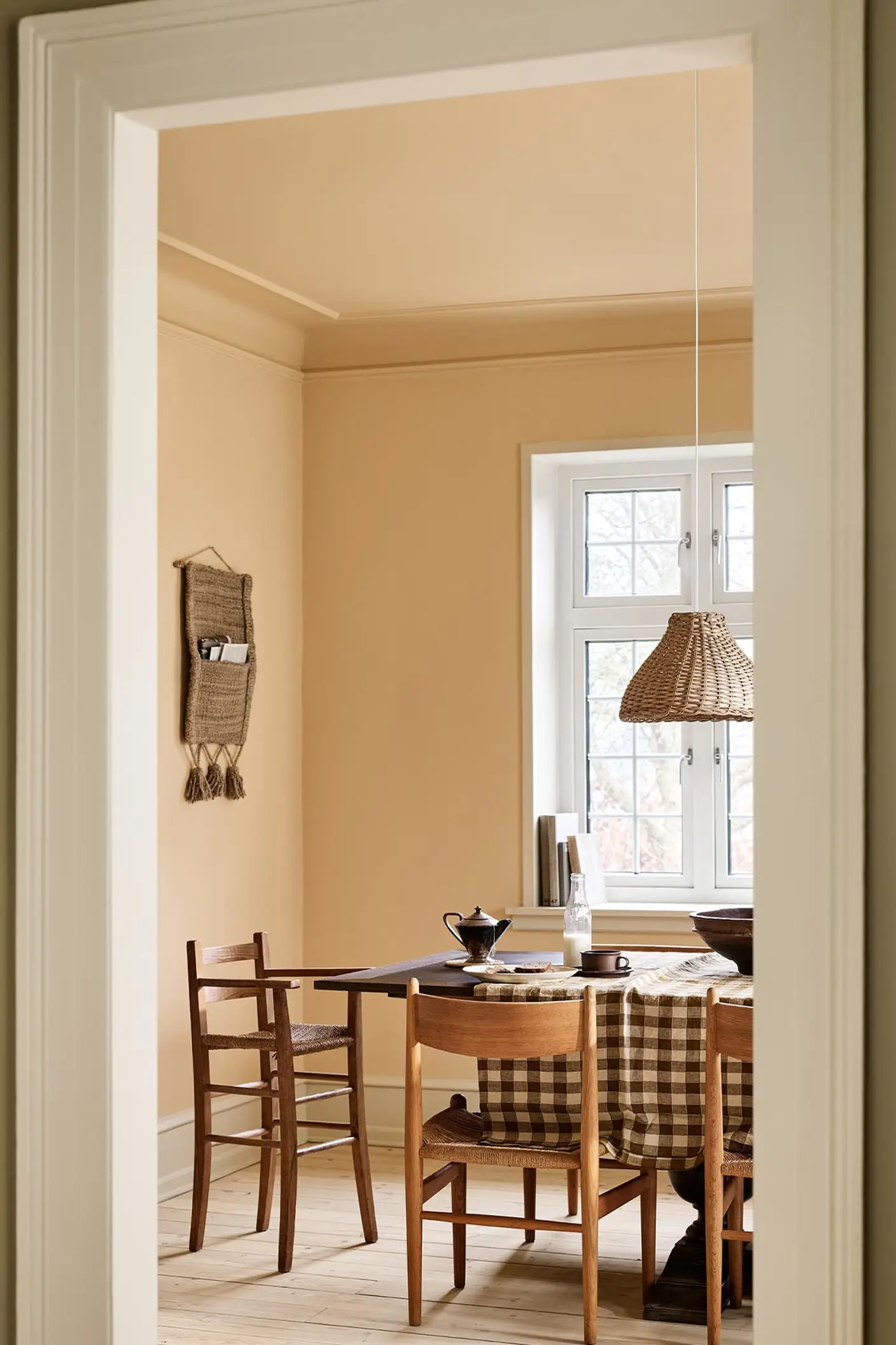 Dining area with a checkered tablecloth, wooden chairs, and ochre coloured walls and ceiling painted with Jotun's 11202 Mild Ochre.
