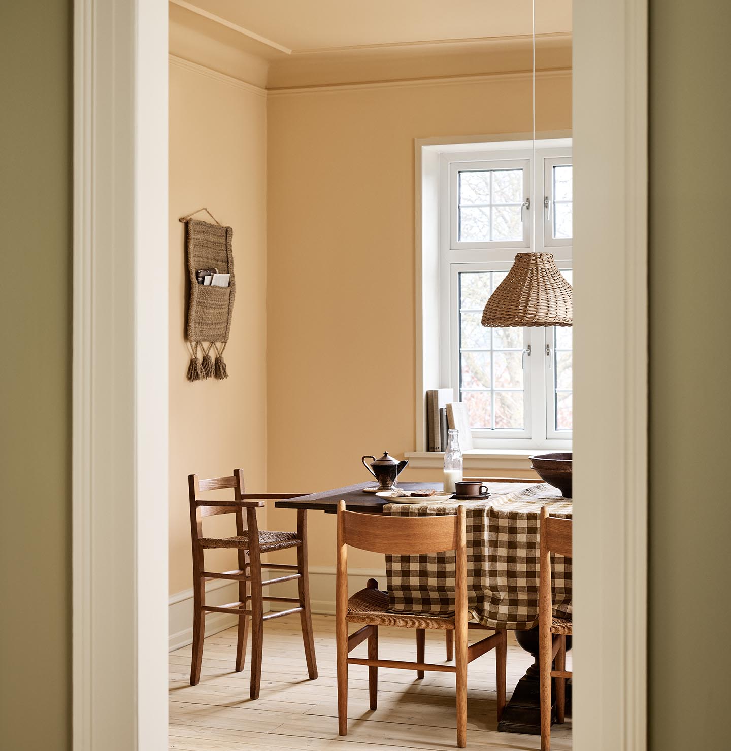 Dining area with a checkered tablecloth, wooden chairs, and ochre coloured walls and ceiling painted with Jotun's 11202 Mild Ochre.