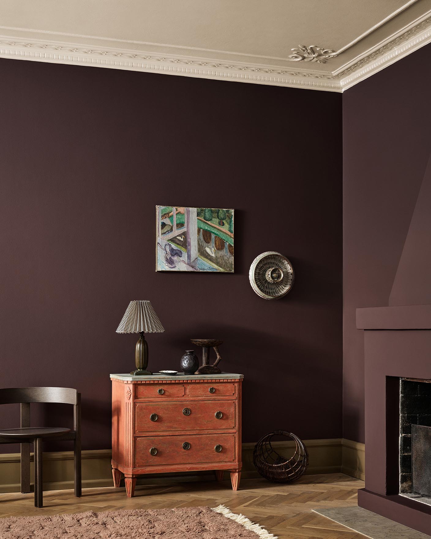 A red dresser, wall art, and fireplace against a deep, brownish red wall painted with the colour Jotun 2149 Coffee.