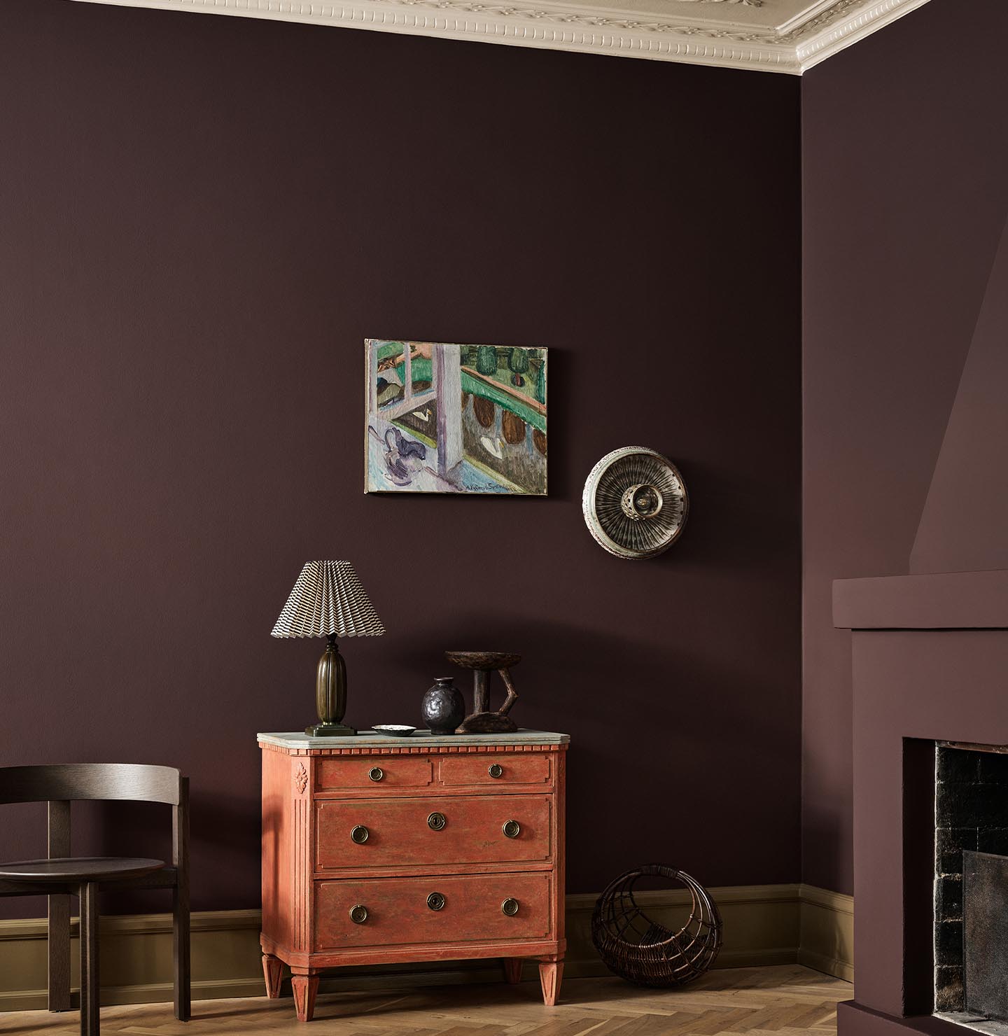 A red dresser, wall art, and fireplace against a deep, brownish red wall painted with the colour Jotun 2149 Coffee.